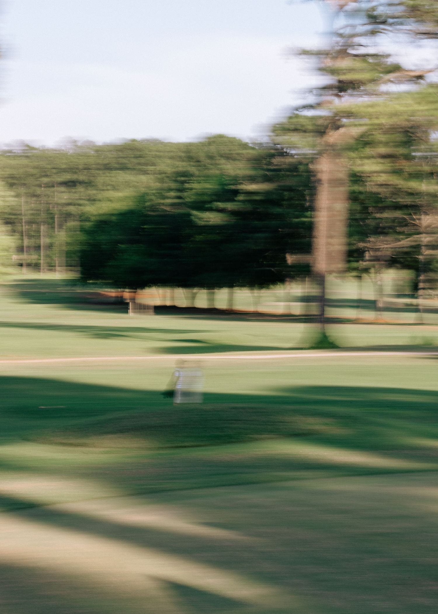Motion blur photo of lush green golf course fairway lined with tall trees.