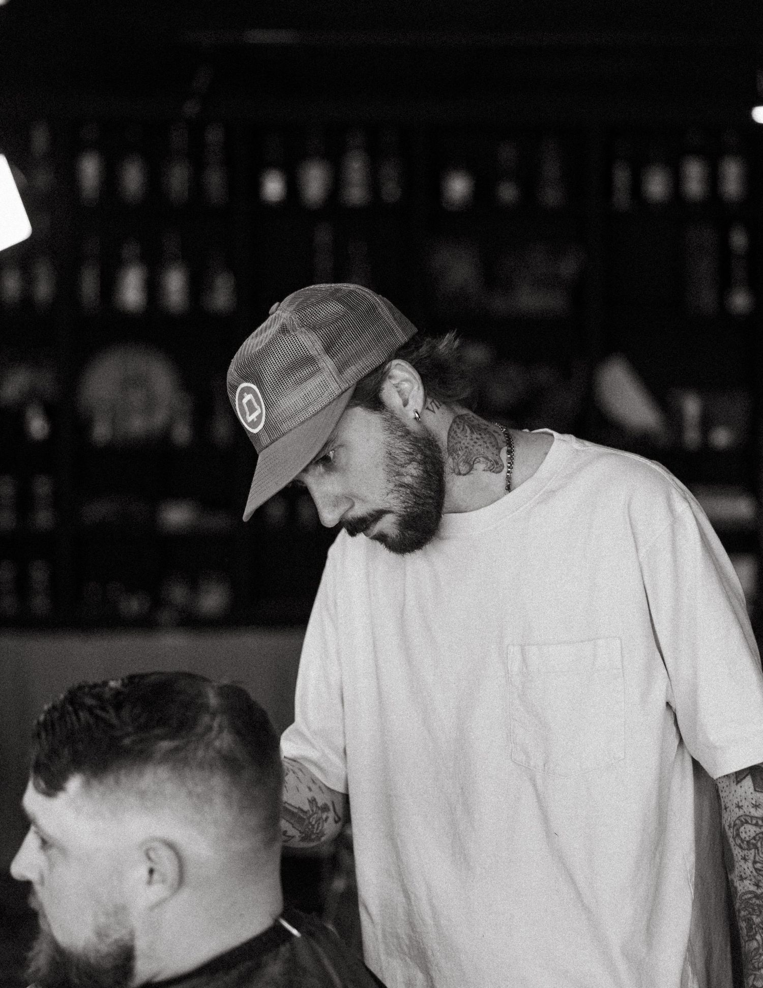 Black and white photo of a tattooed barber in a cap focusing on a client's haircut.