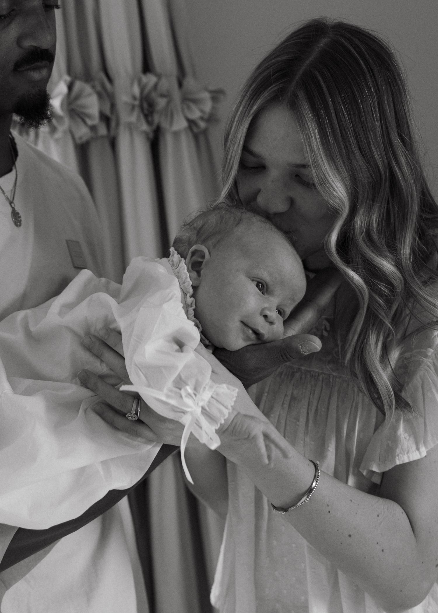 Black and white photo of a mother kissing her newborn baby held by father.