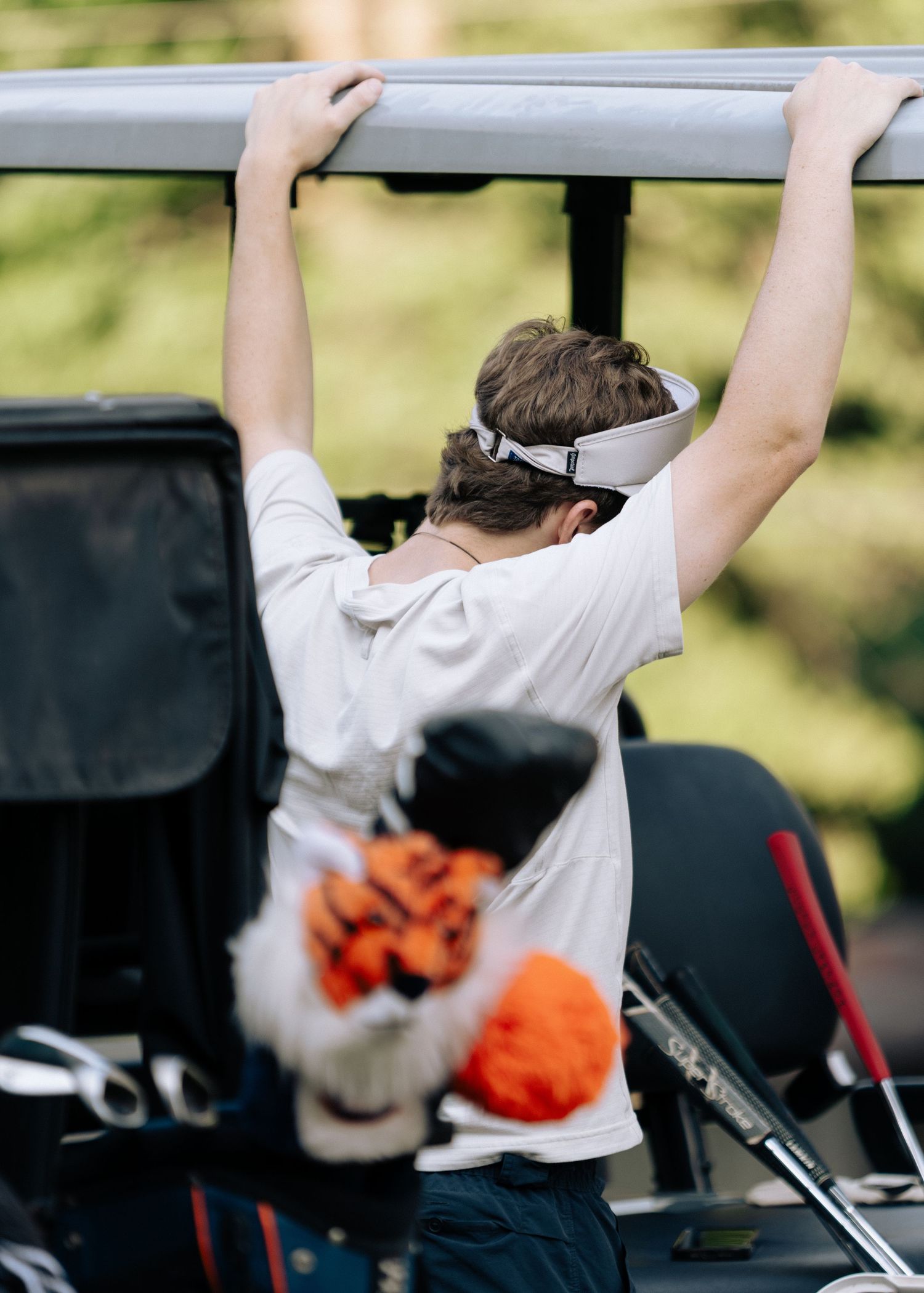 Young man in white shirt reaches up to adjust golf cart roof from behind.