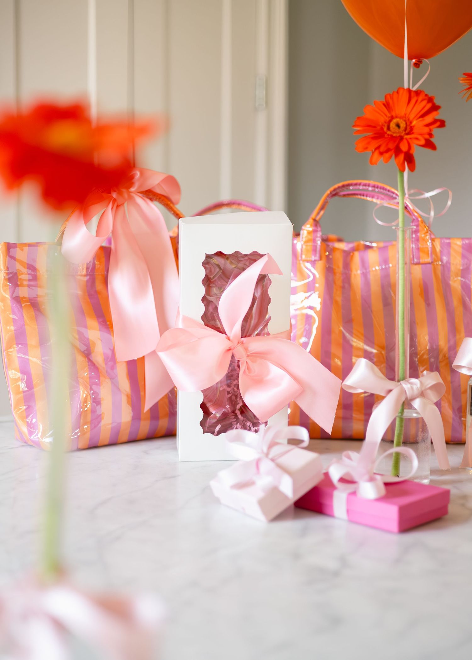 Orange and pink striped gift bags with pink satin bows on a marble surface.
