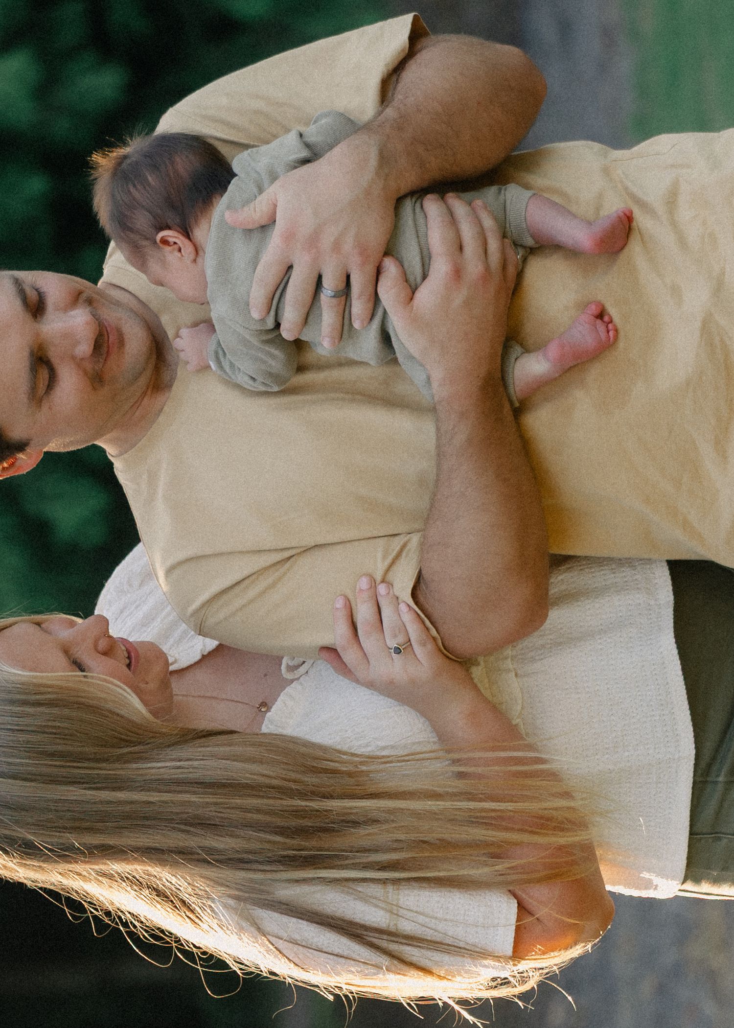 Parents together holding their newborn baby in golden hour outdoor light.