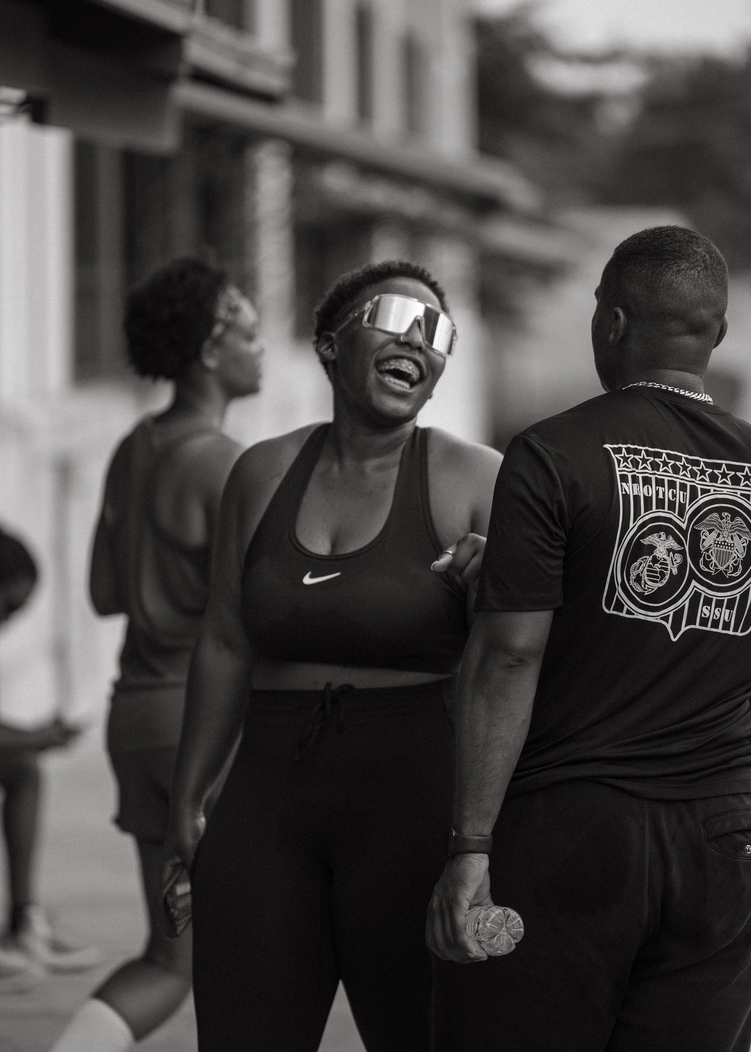 Black and white photo of a laughing woman in Nike sports bra with mirrored sunglasses outdoors.
