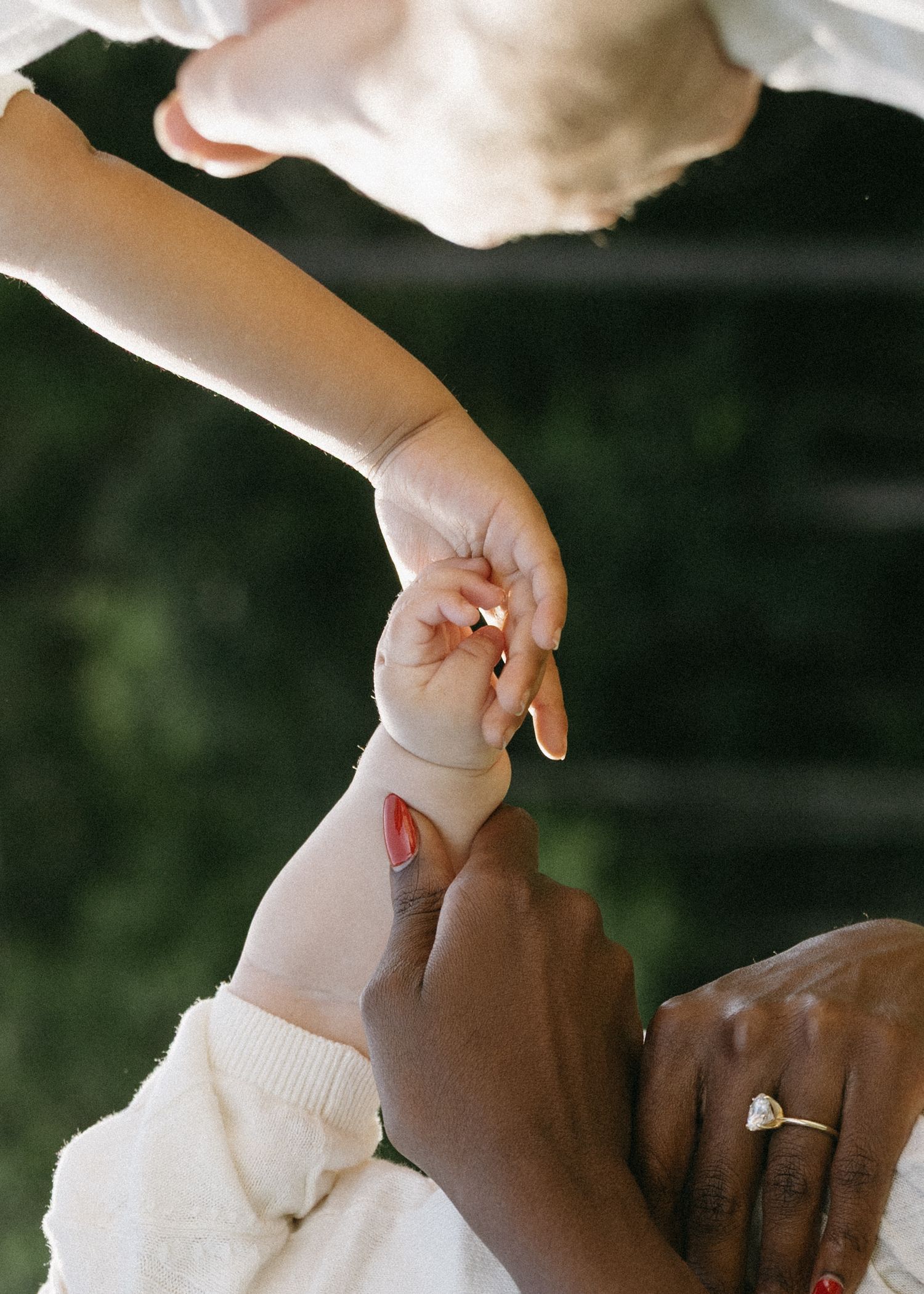 A mother with a diamond ring gently holds her baby's tiny hand outdoors.