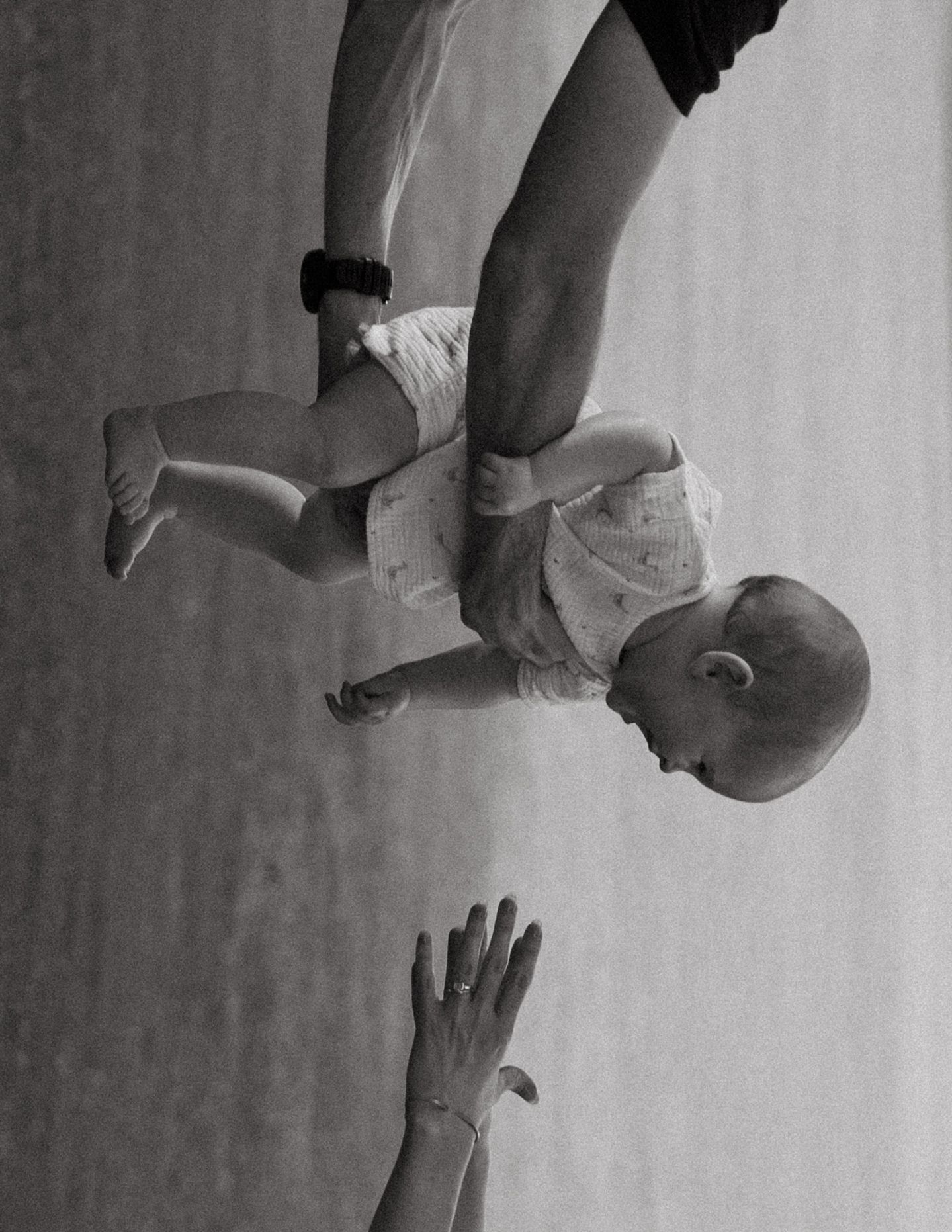 Black and white photo of a parent lifting a baby overhead outdoors.