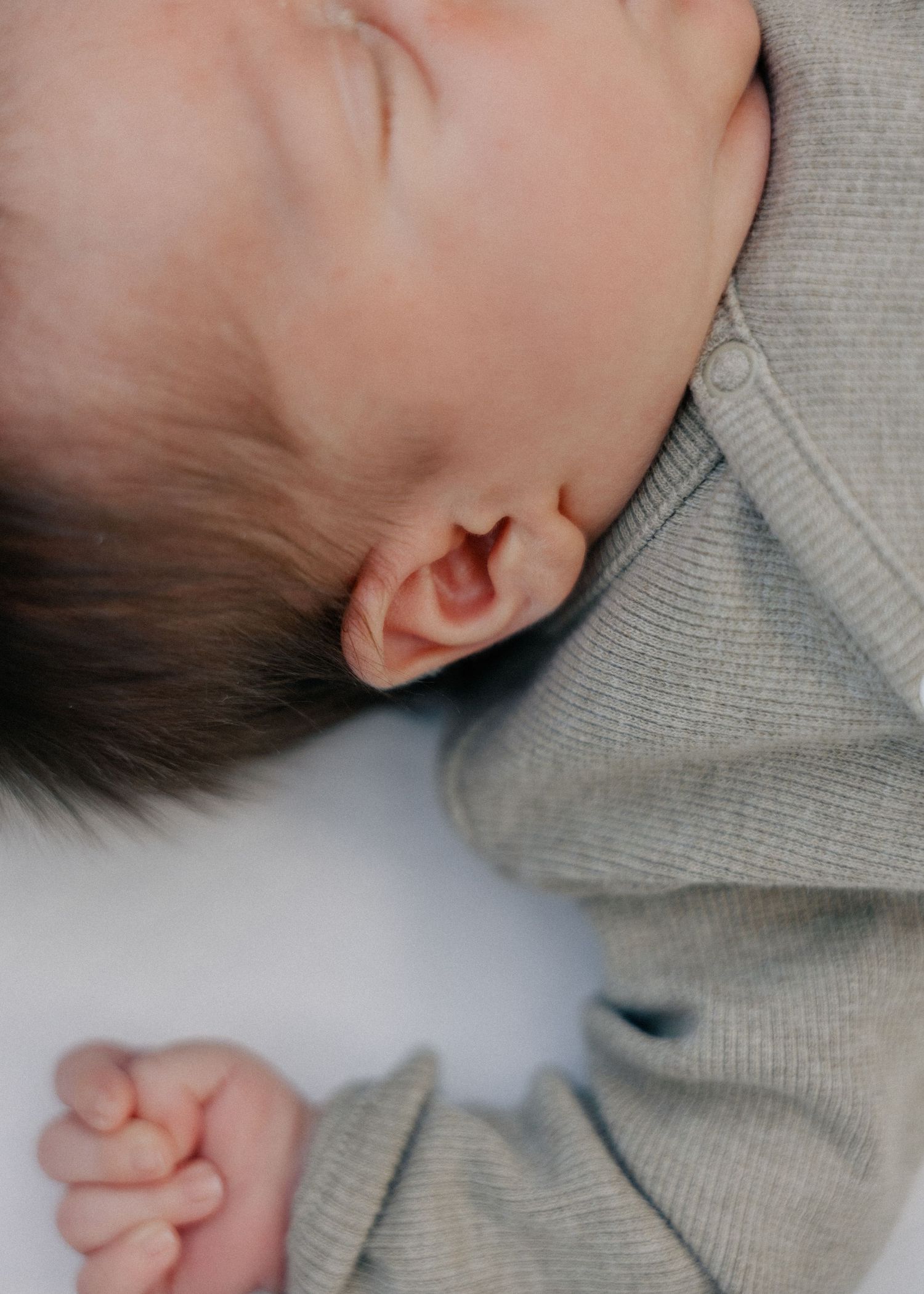 Close-up of a sleeping newborn baby in a soft gray knit outfit.
