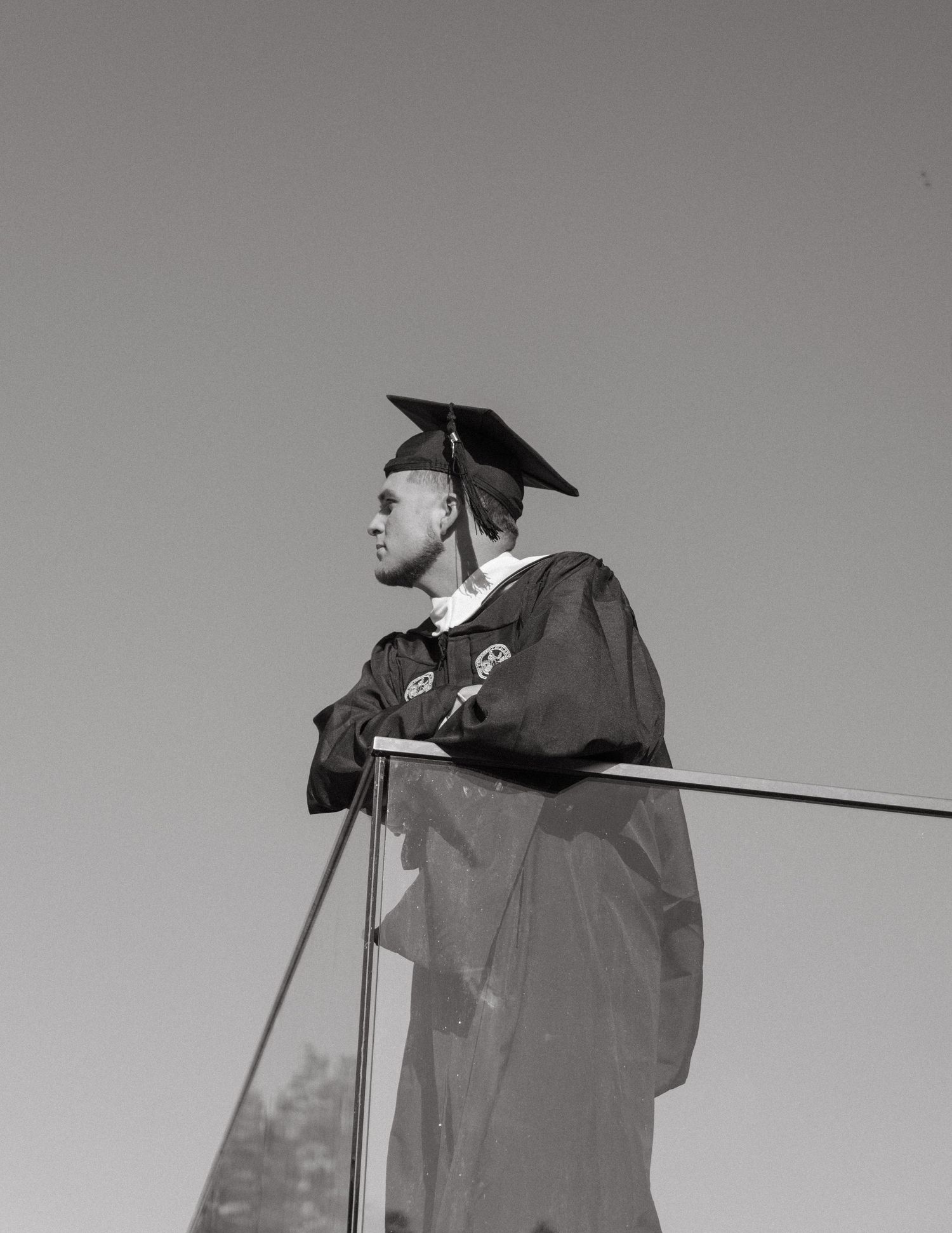 Graduate in cap and gown standing at podium during outdoor graduation ceremony against clear sky.