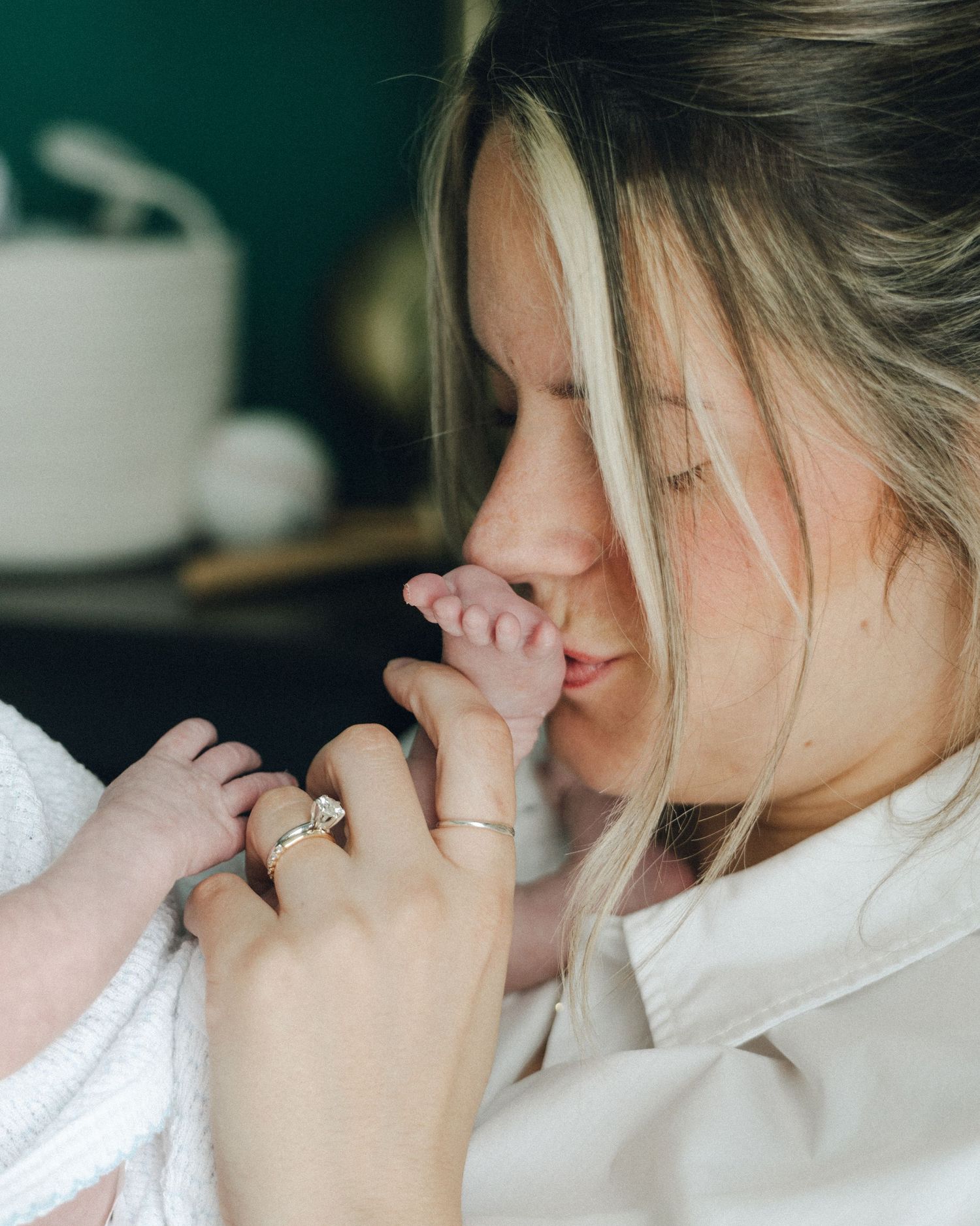 Close-up of mother kissing newborn baby's tiny feet while wearing engagement ring.