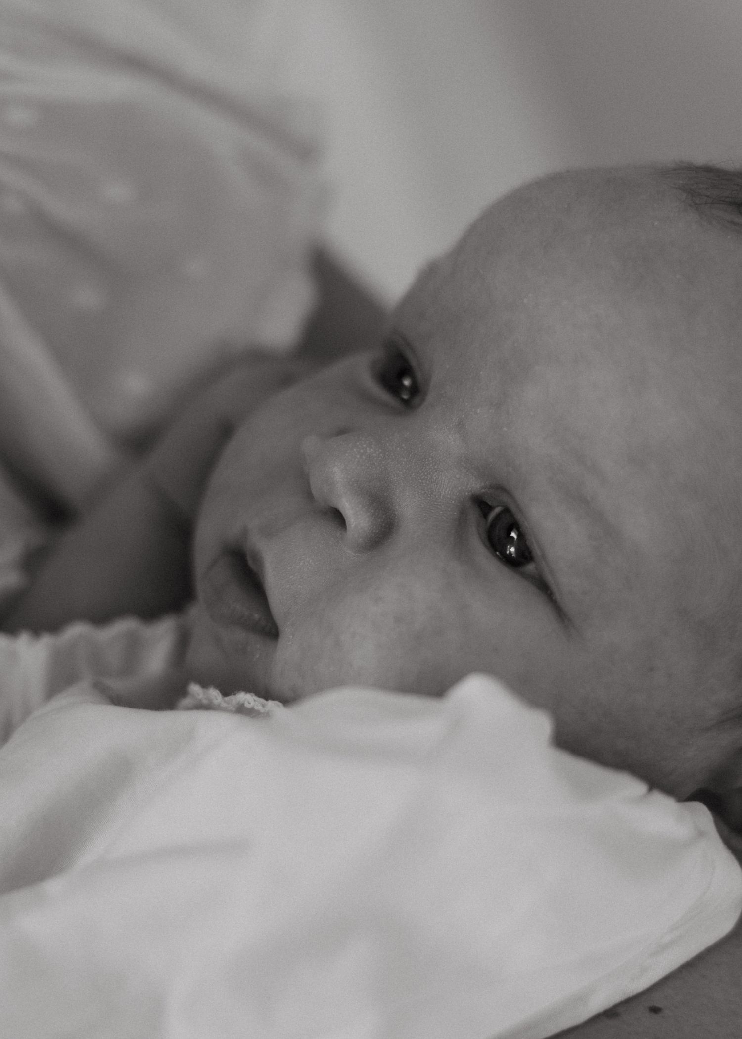Close-up black and white portrait of a newborn baby lying on a soft white blanket.