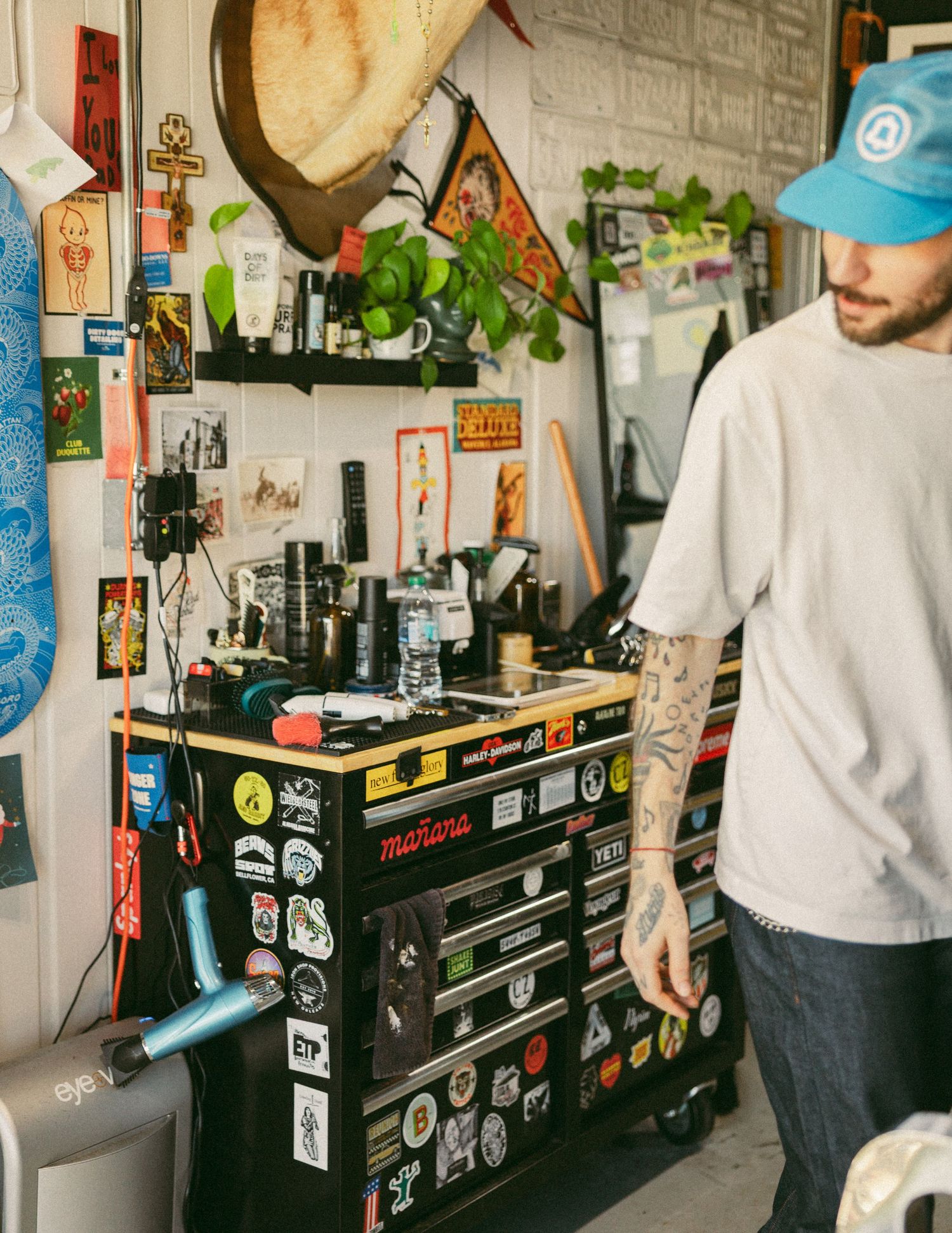 Tattooed man standing near a tool chest covered in stickers in a creative workspace.