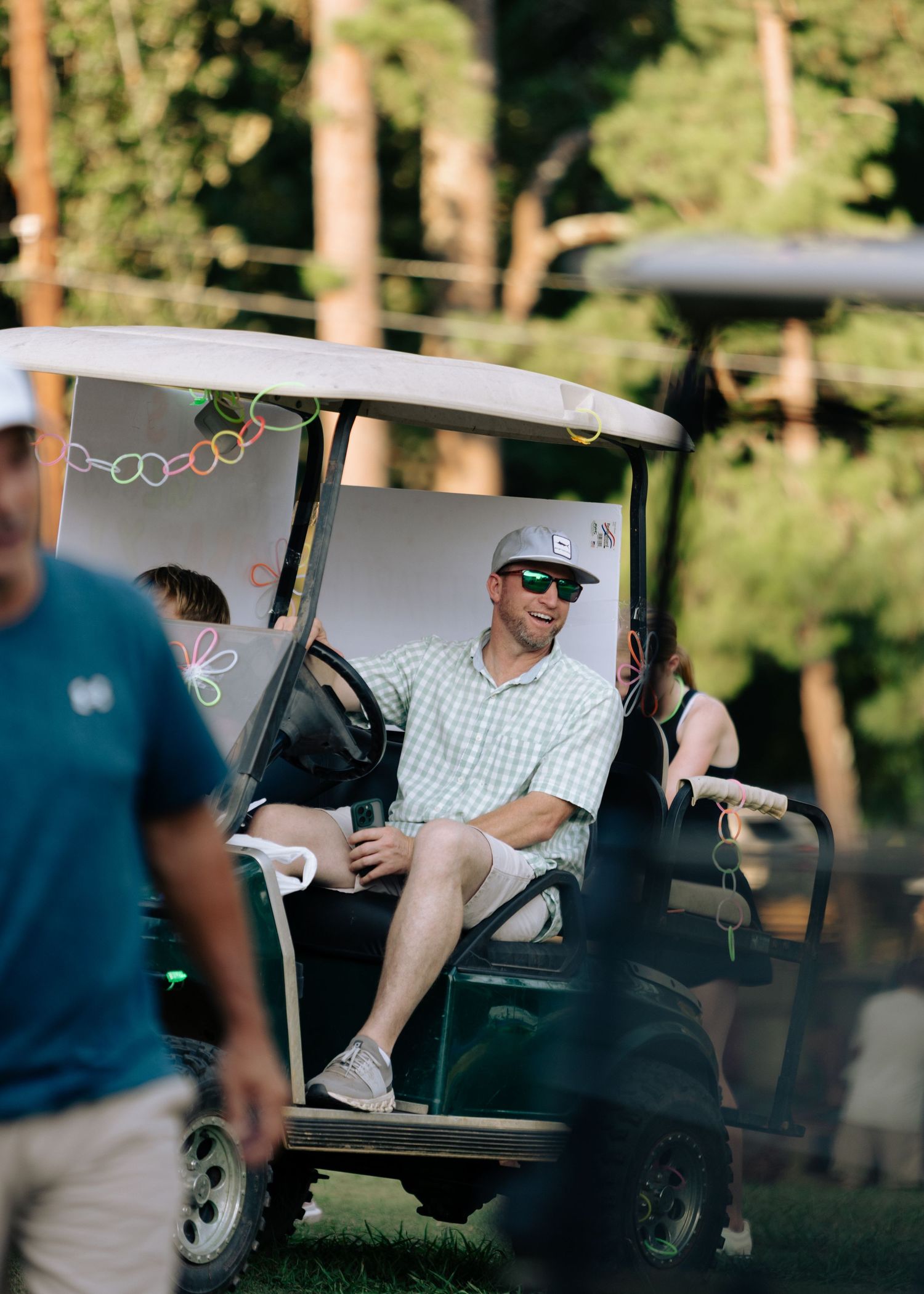 Smiling man in sunglasses and cap relaxing in a decorated golf cart outdoors.