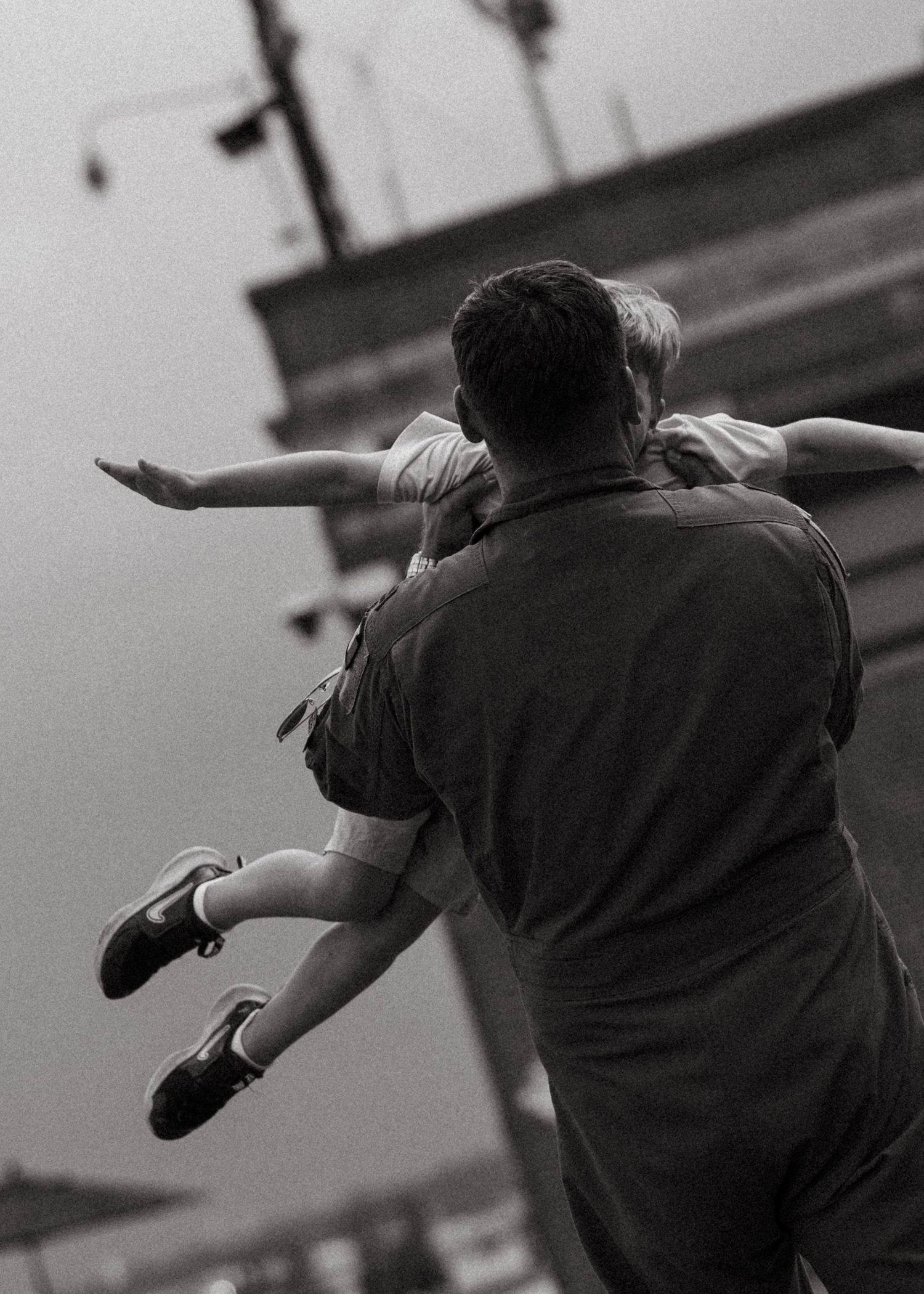 Vintage black and white photo of a man in uniform playfully lifting a child with arms outstretched like an airplane.