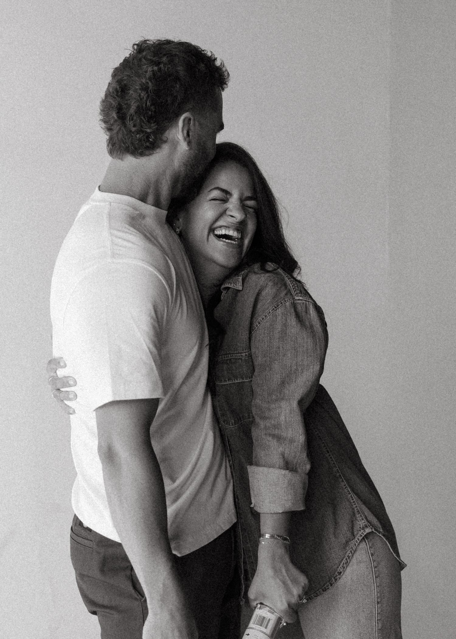 Black and white photo of couple laughing and embracing joyfully during a pregnancy announcement photoshoot.