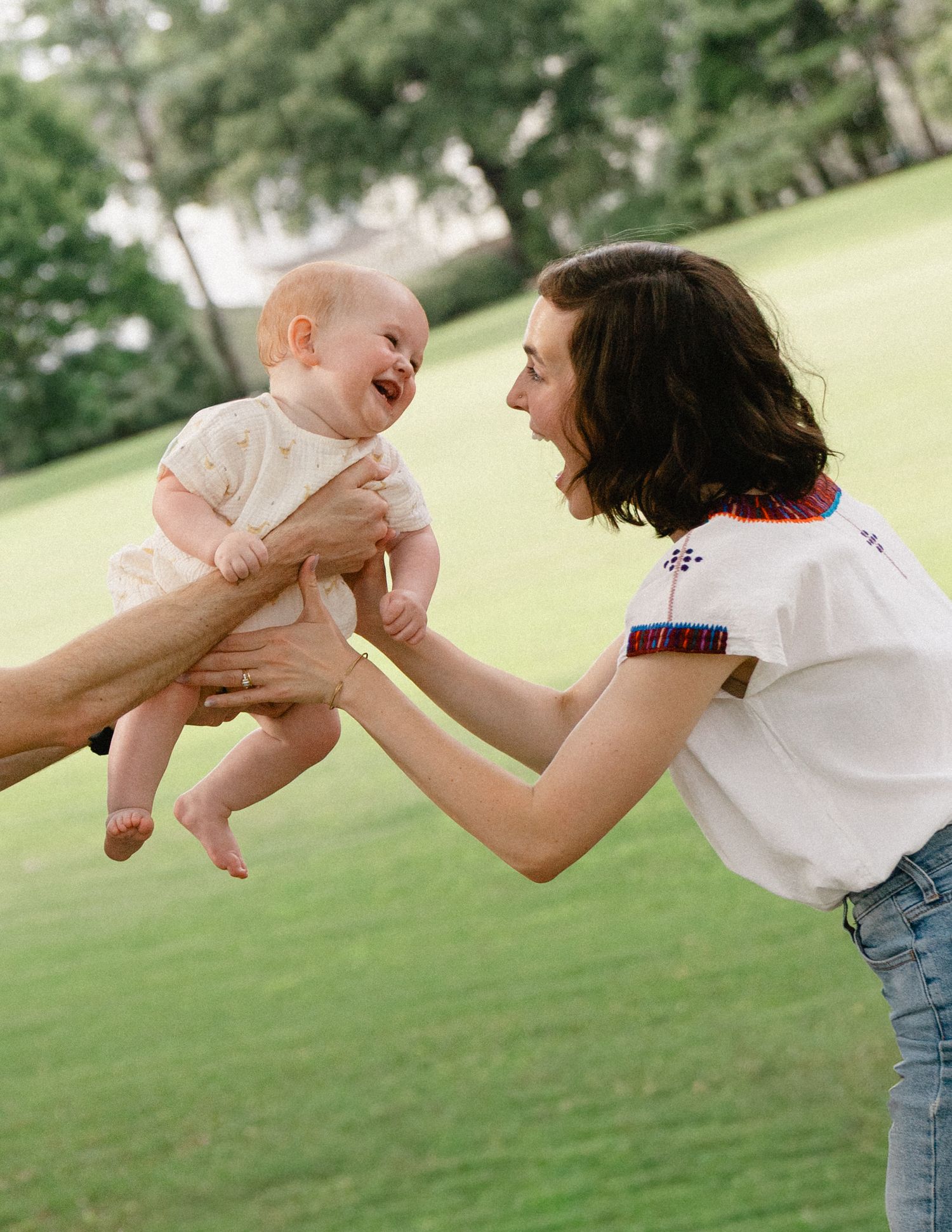 A joyful mother lifts her laughing baby in a sunny green park.