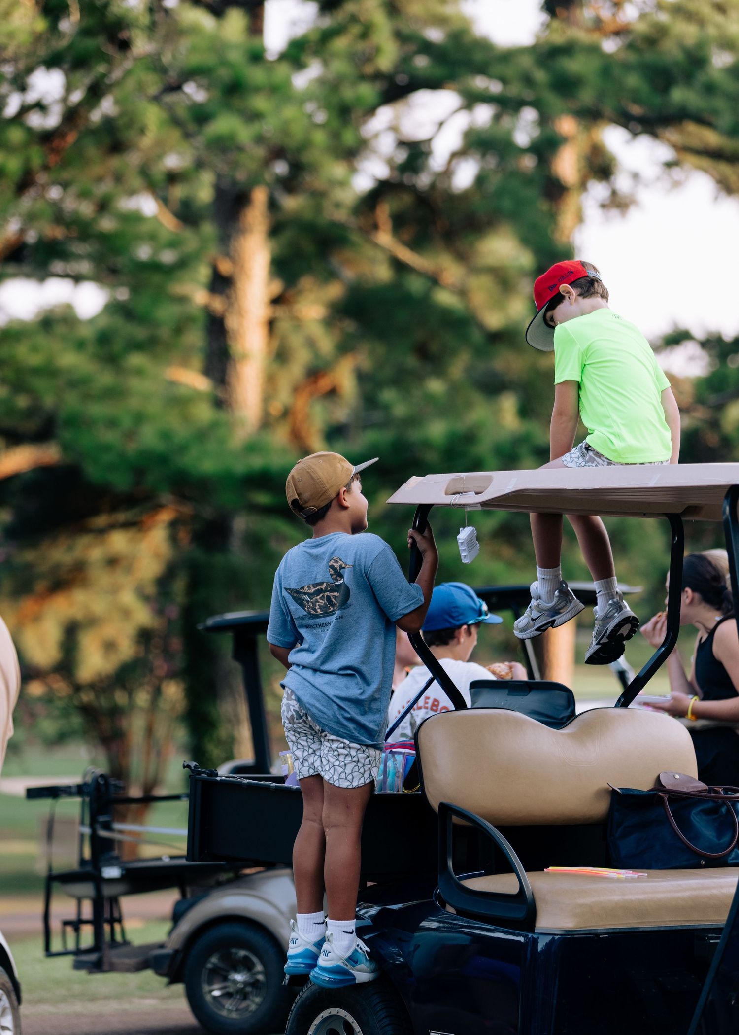 Group of kids gathered around a golf cart at sunset on a golf course.