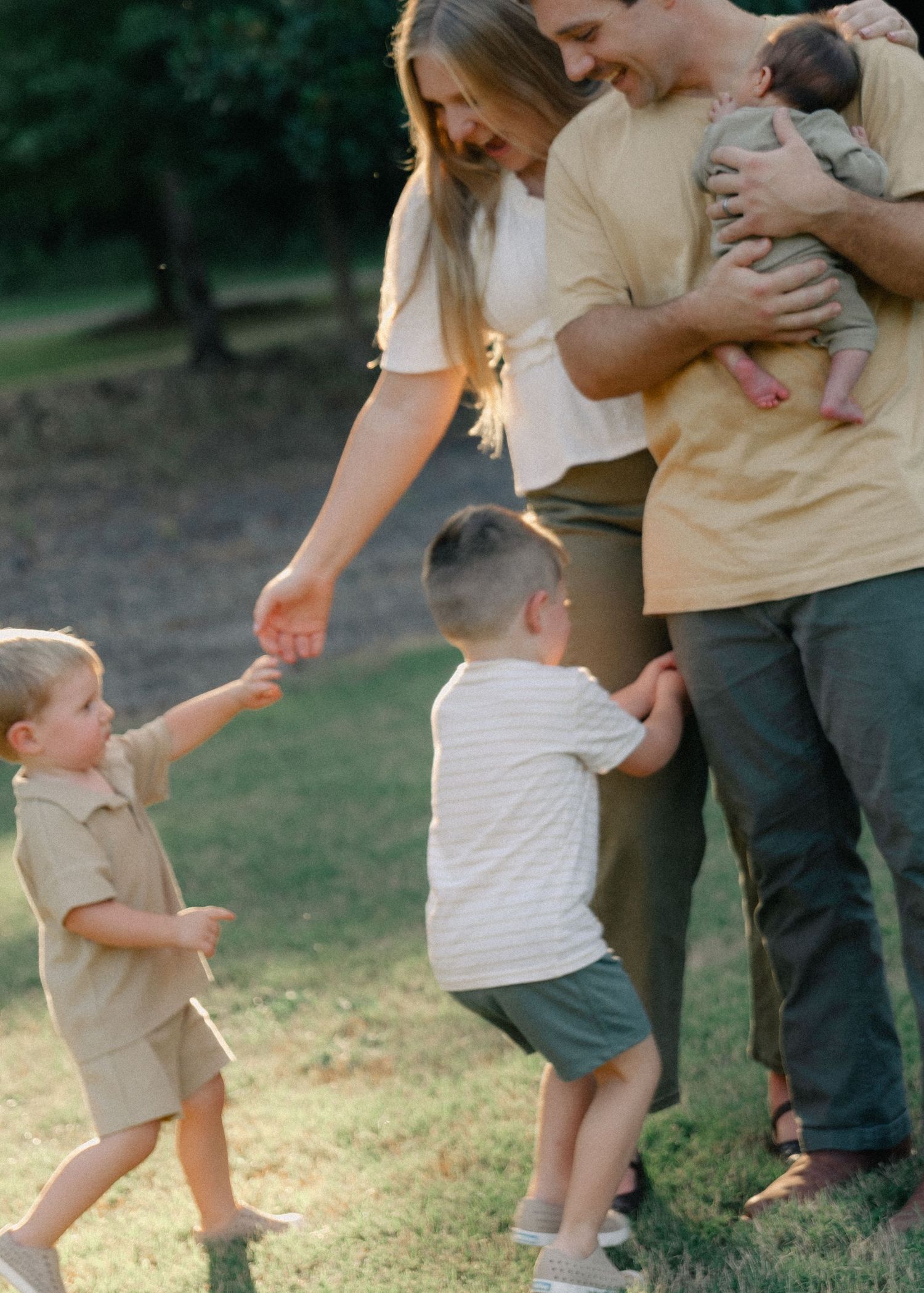 Happy family with two toddlers and a newborn enjoying time together in a park.