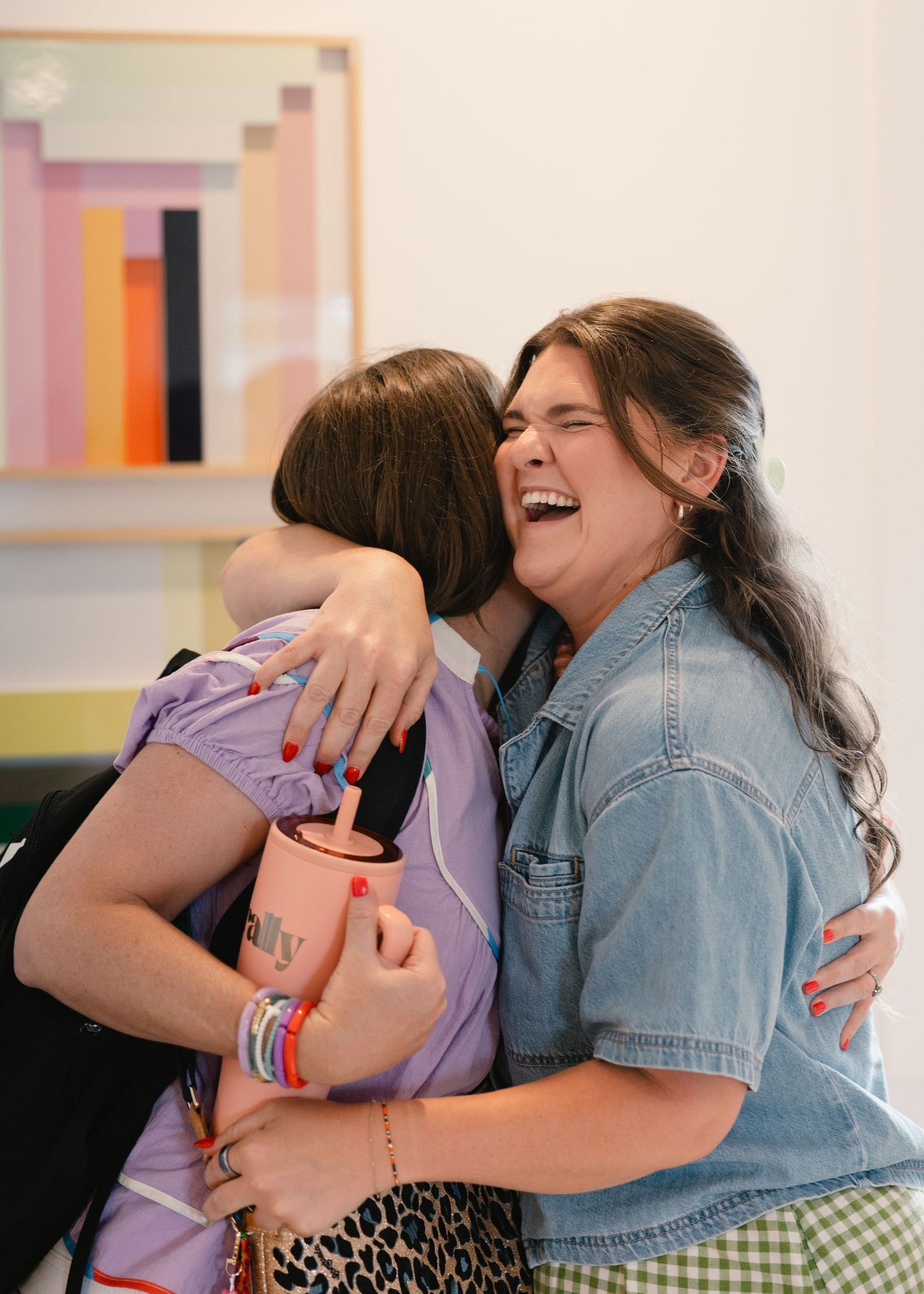Two women sharing a joyful hug and laughing at a colorful indoor event.