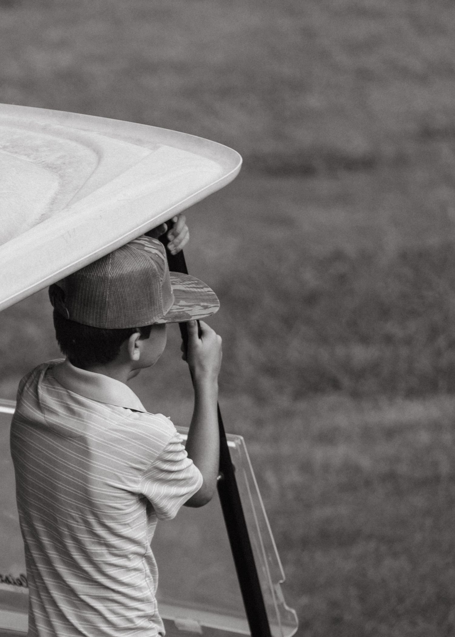 Young boy in cap sitting in golf cart viewed from behind in black and white.