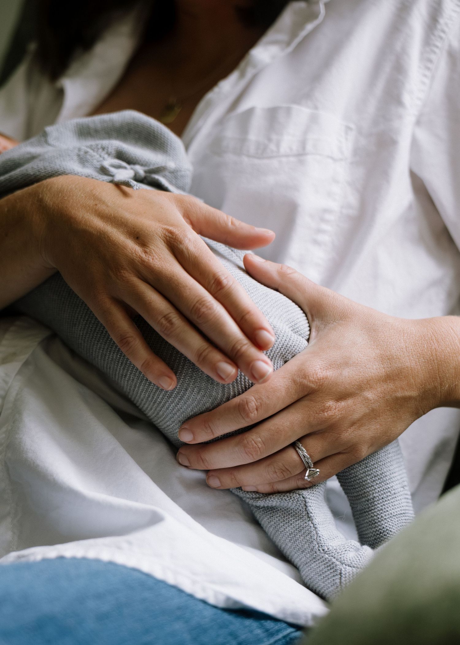 Close-up of mother's hands gently holding swaddled newborn baby, wearing diamond engagement ring.