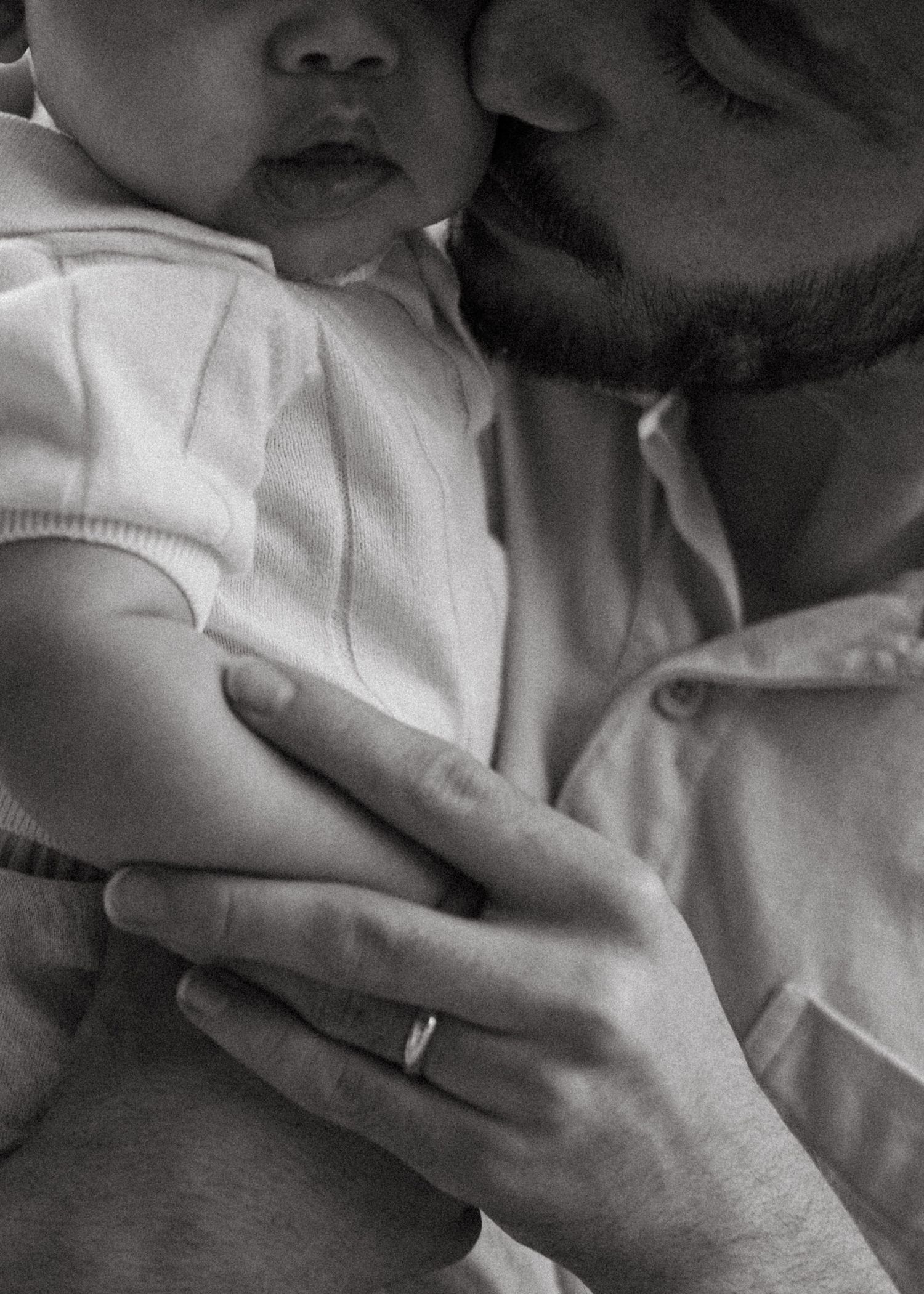 Black and white close-up of a bearded father tenderly kissing his newborn baby.