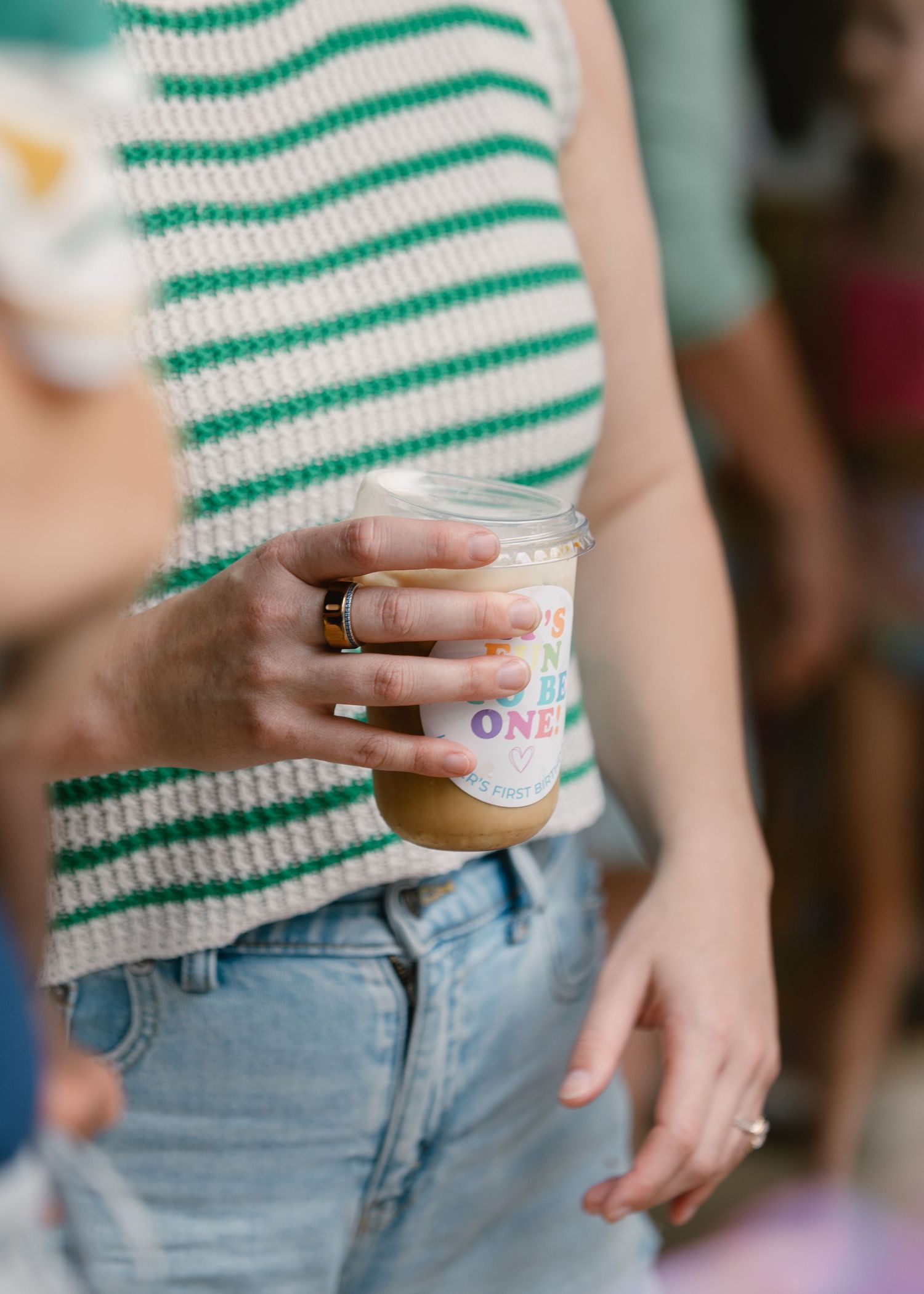 Woman in green striped knit top holding a clear cup with Its Fun to Be One printed on it.