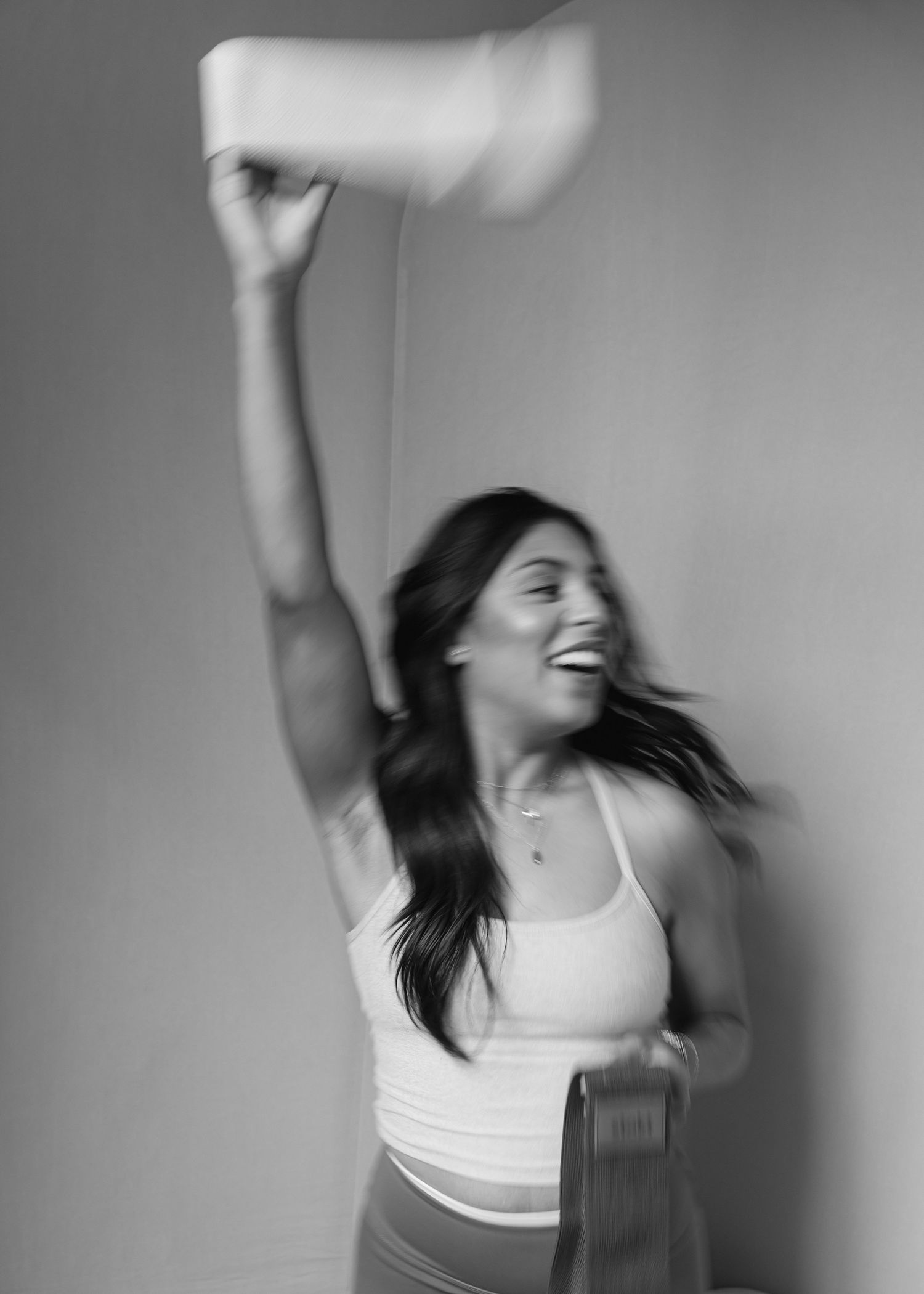 Woman in white tank top joyfully tossing a hat in the air, black and white motion blur photo.