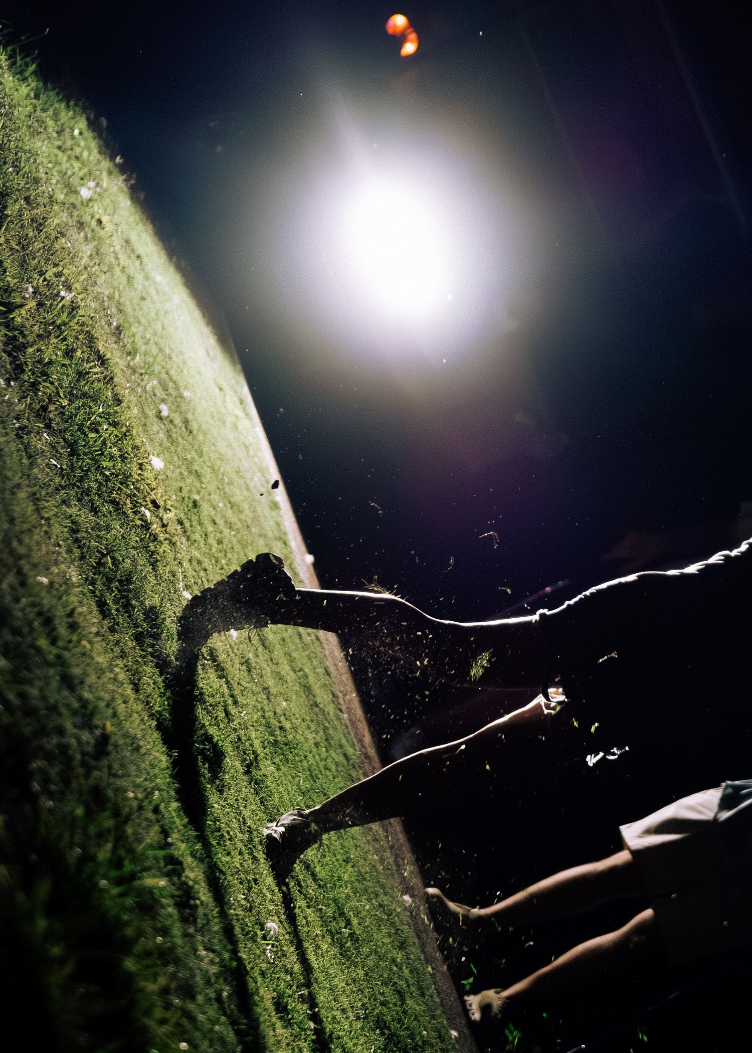 Dramatic night golf shot with bright light illuminating a golfer's shadow on green grass.