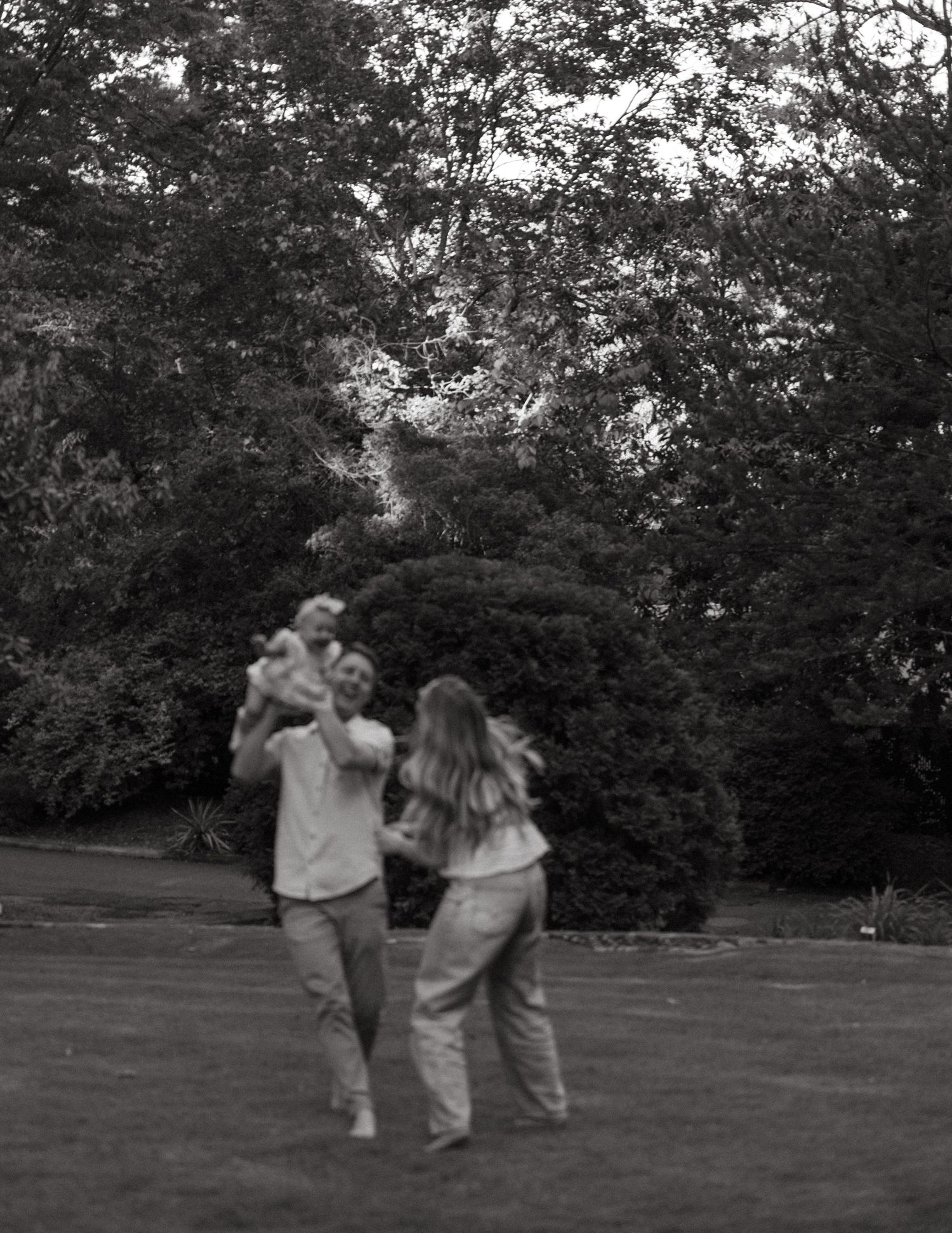 Black and white photo of family playing with baby in lush garden.