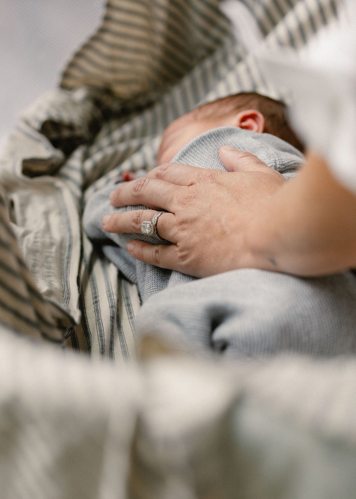 Mother's ringed hand gently resting on swaddled newborn baby in striped blanket.