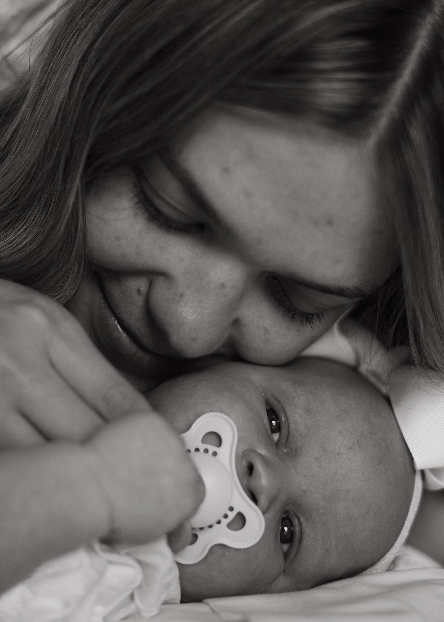 Black and white close-up of mother nuzzling her newborn baby with pacifier.