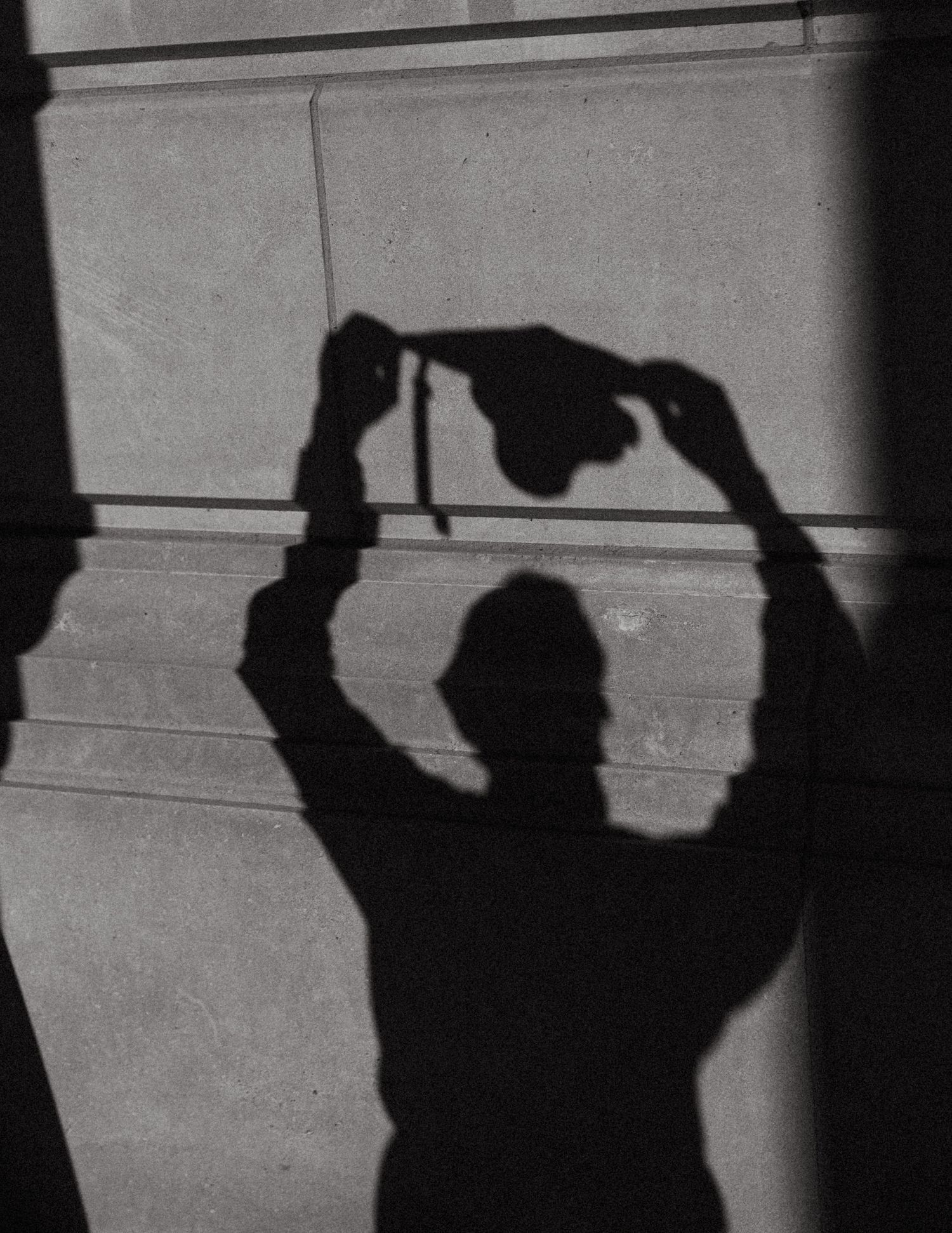 Artistic shadow silhouette of a photographer holding a camera above their head against a concrete wall.