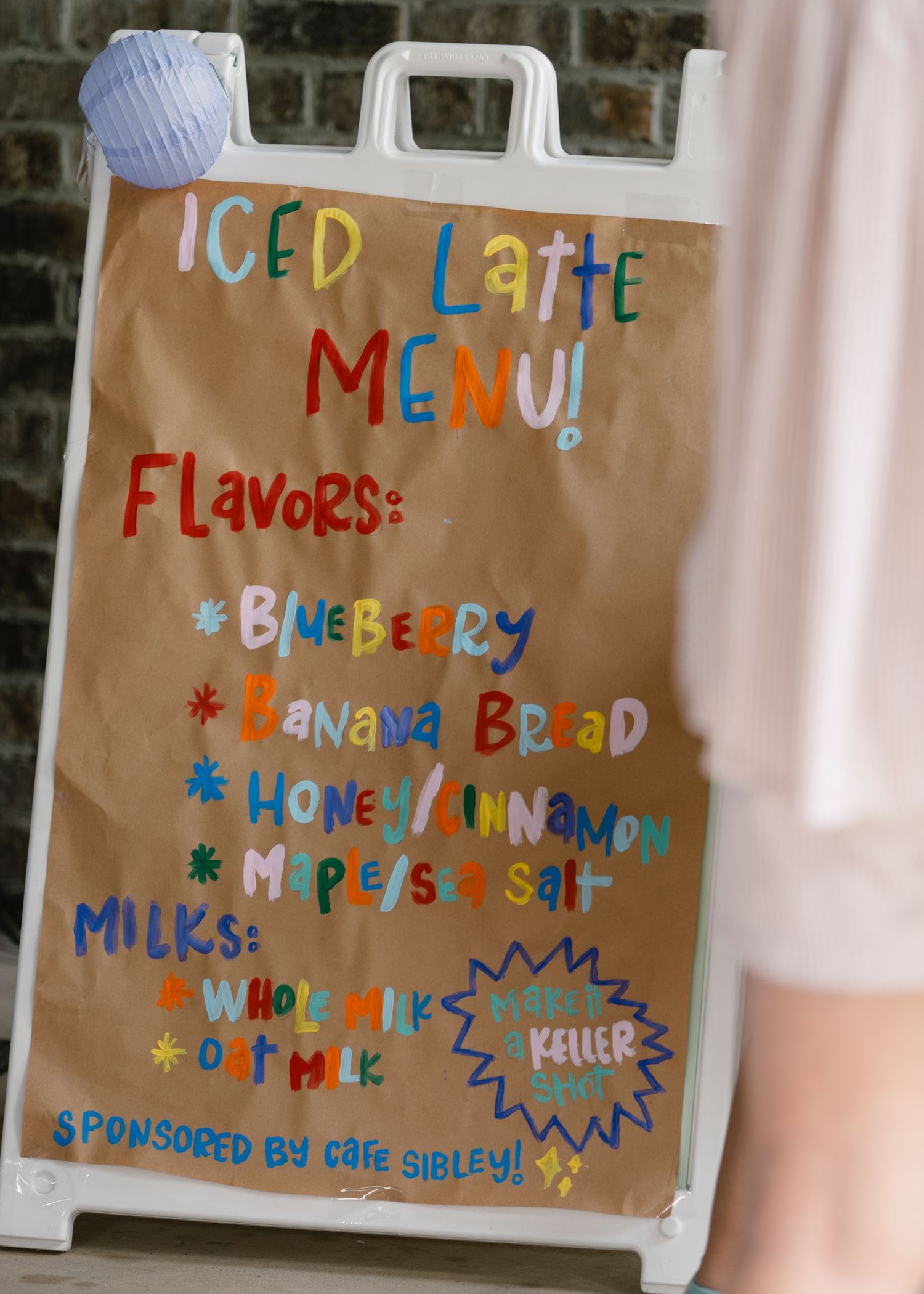 Handwritten iced latte menu sign listing blueberry, banana bread, honey cinnamon, and maple sea salt flavors.