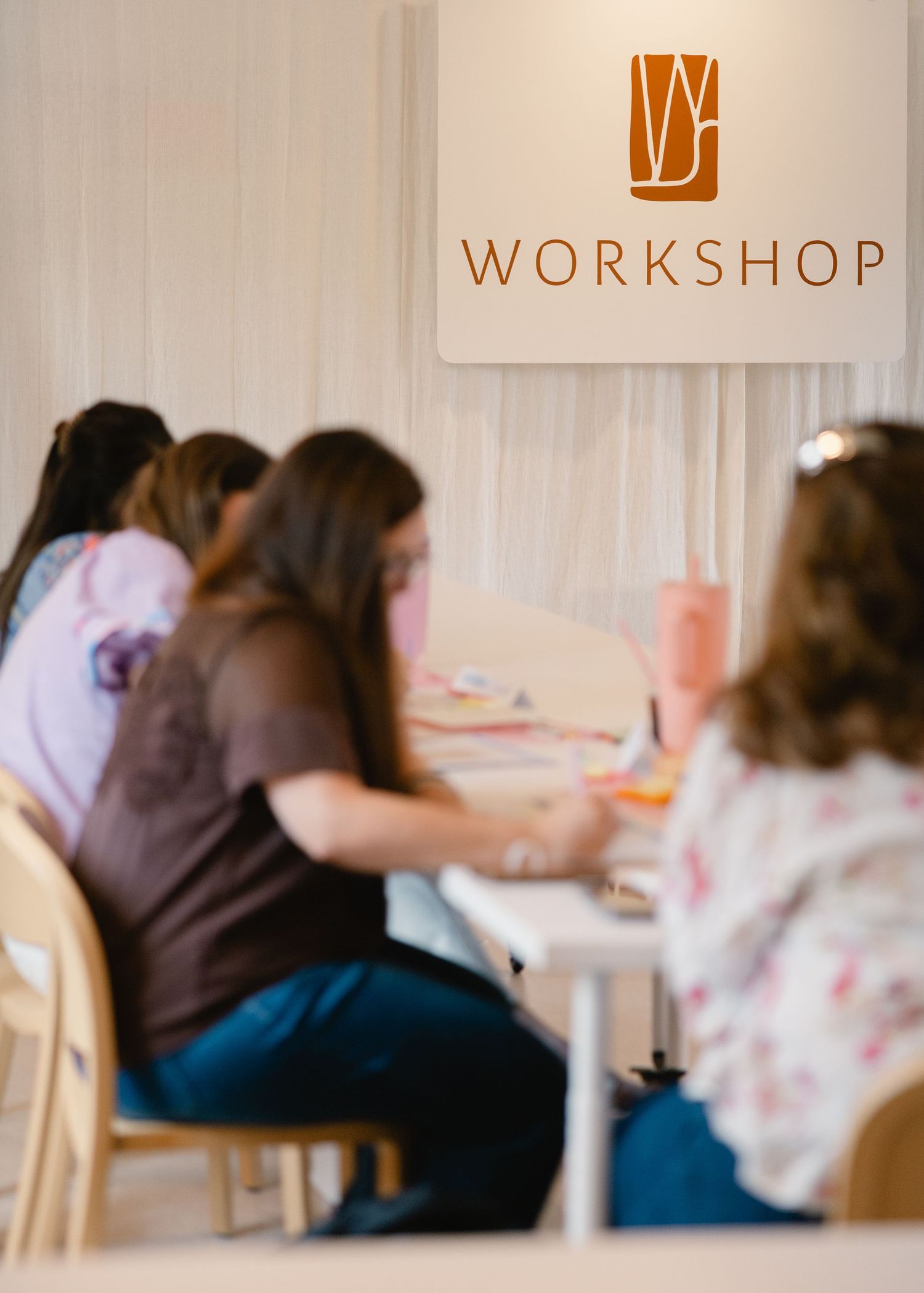 Attendees working at tables beneath a Workshop logo sign in a bright event space.