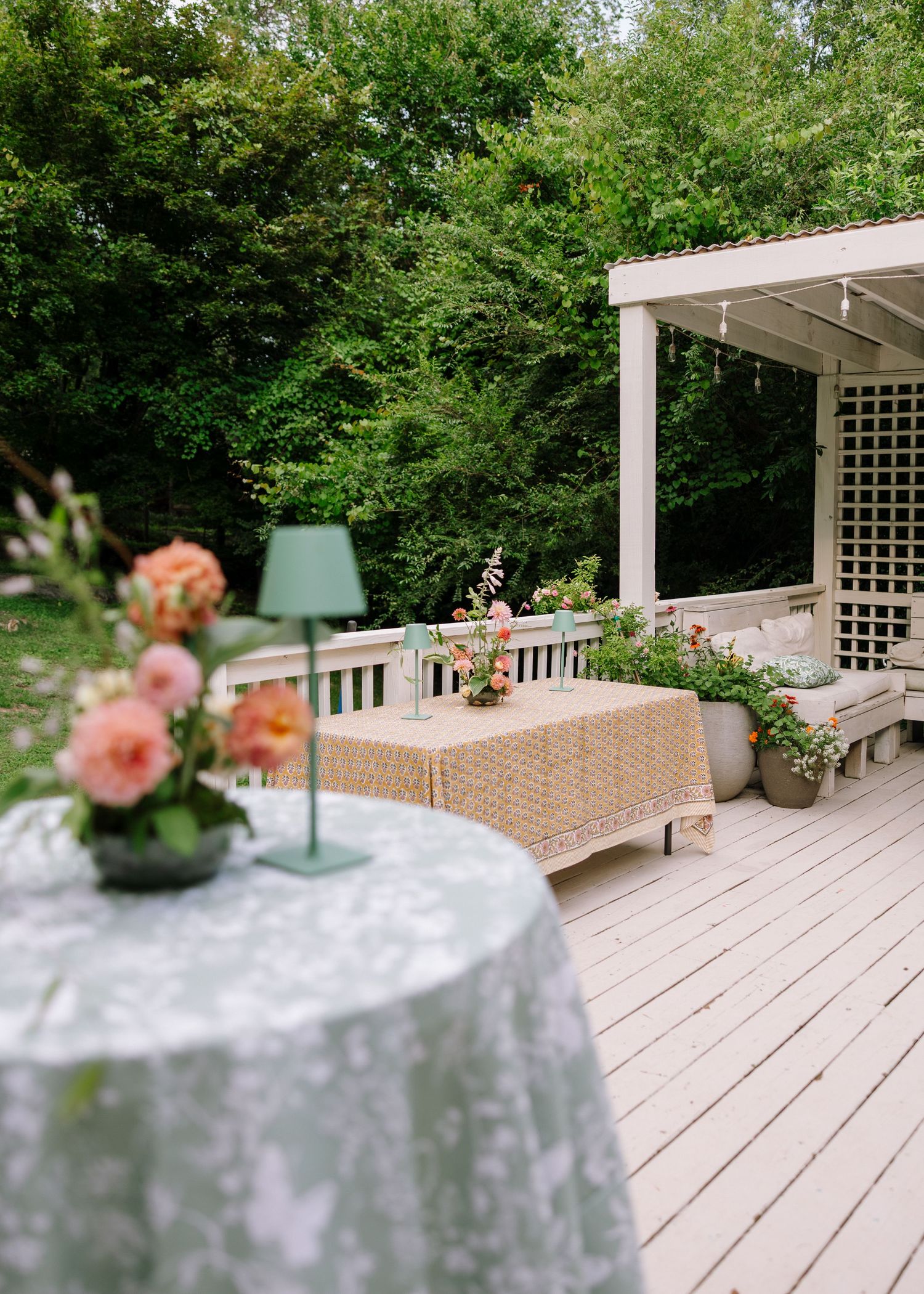 Elegant outdoor deck with floral centerpieces, string lights, and lush green garden backdrop.