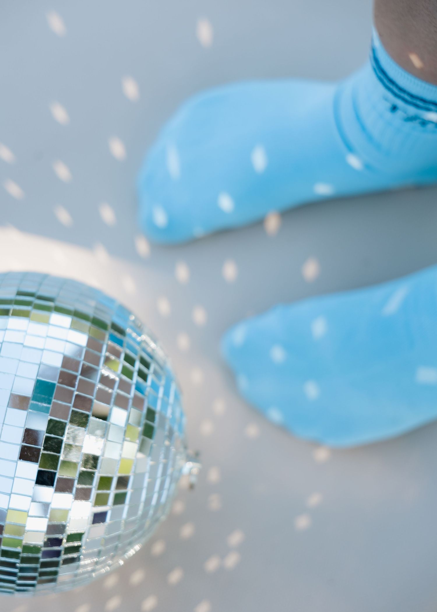 Blue polka dot socks next to a sparkling disco ball casting light reflections on a gray floor.
