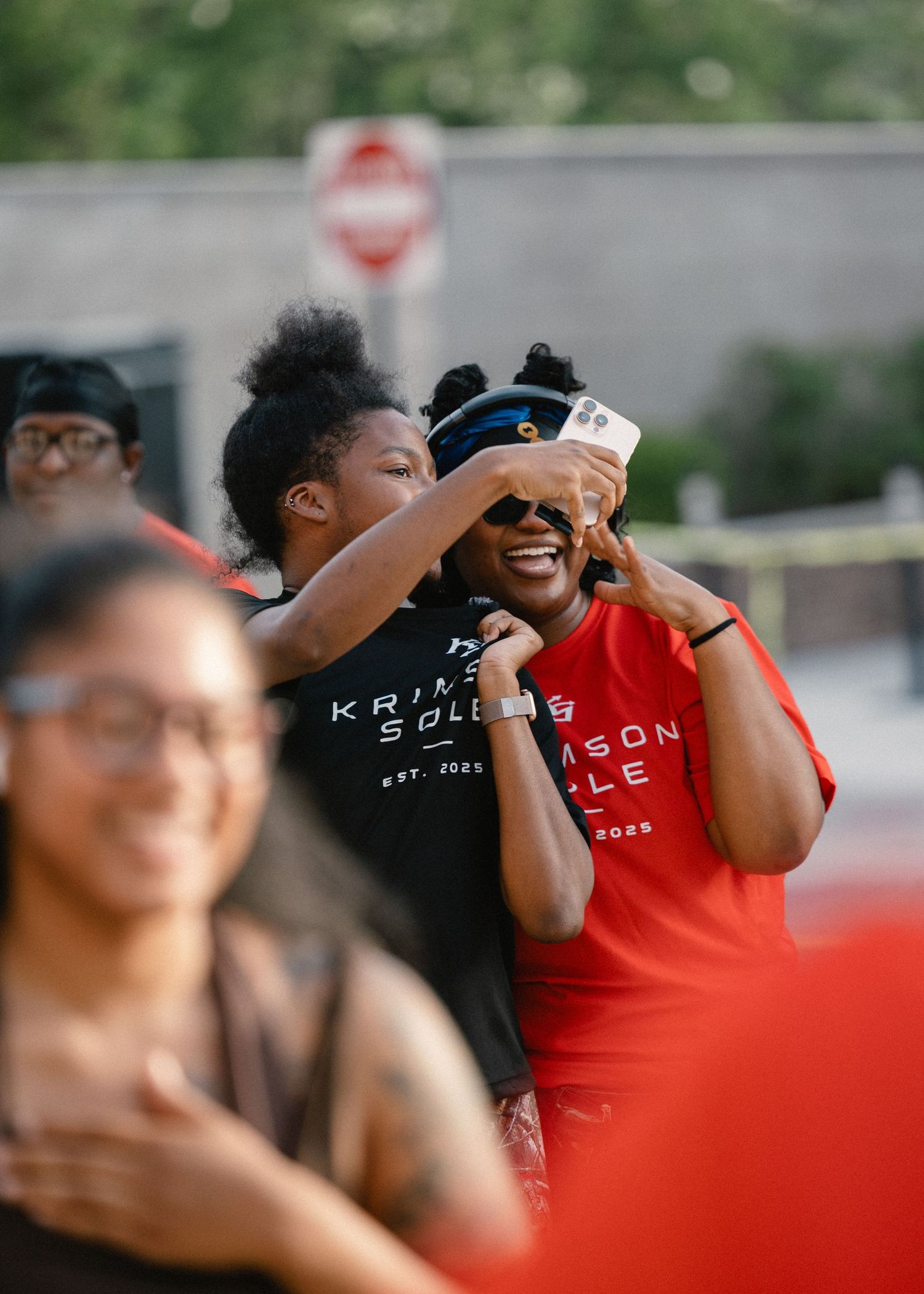 Two women laughing and taking a selfie outdoors at a Krimson Sole running club event.