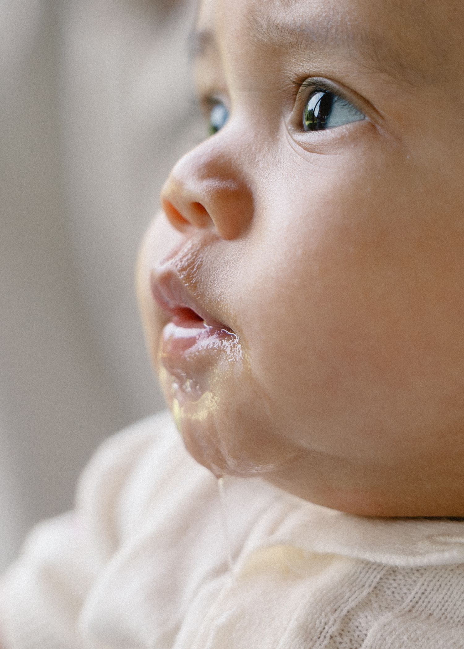 Close-up portrait of an adorable baby with drool on their chin looking upward curiously.