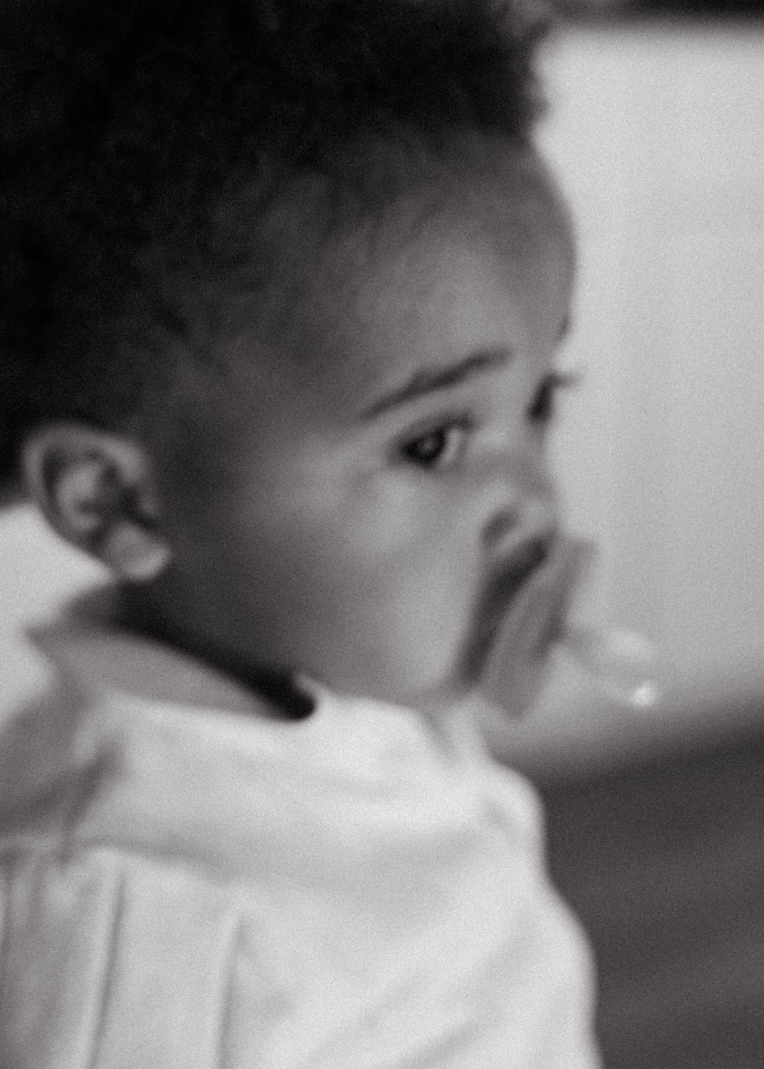Black and white profile portrait of a curious toddler with curly hair looking sideways.