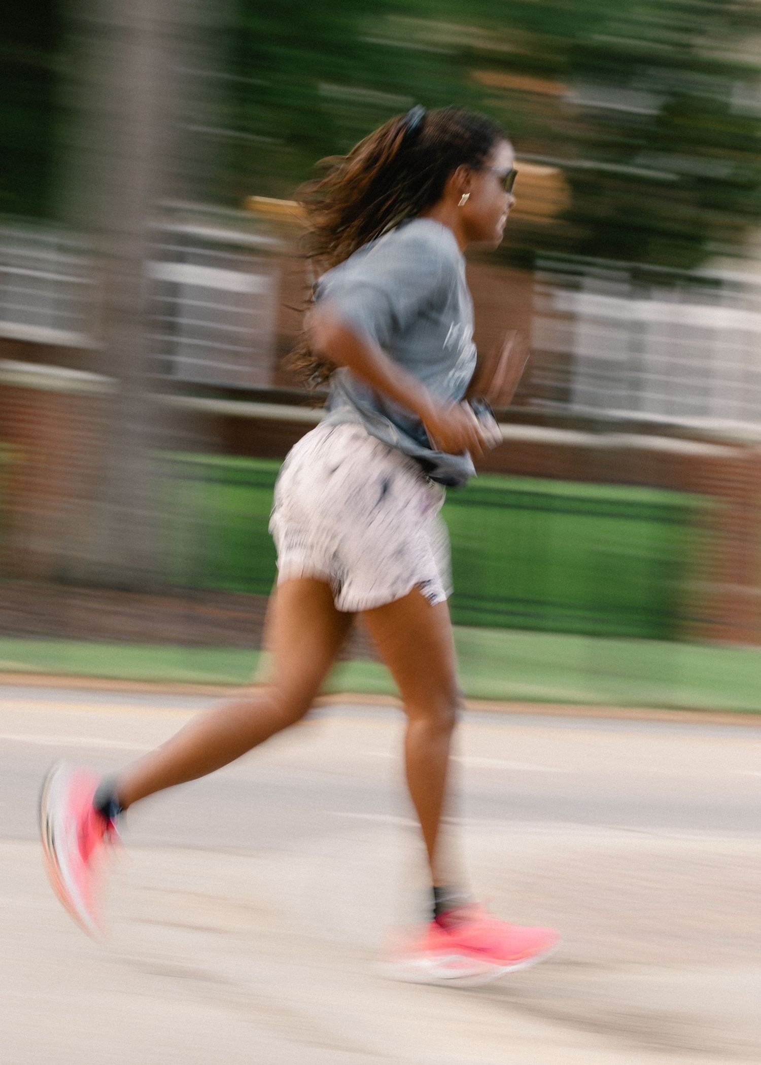 Motion blur action shot of a woman running in pink sneakers and shorts outdoors.