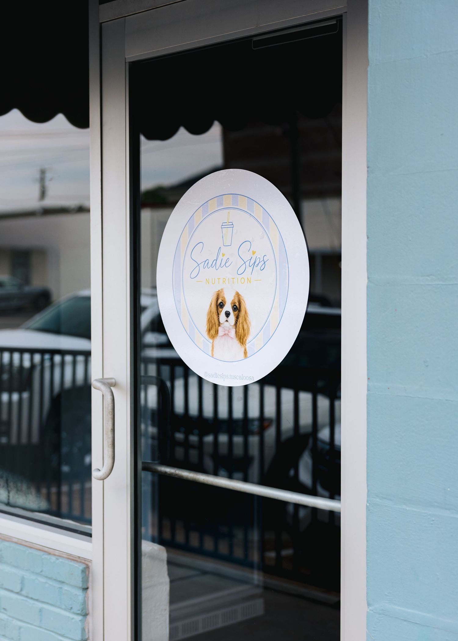 Sadie Sips coffee shop entrance door with oval logo featuring a Cavalier King Charles Spaniel.