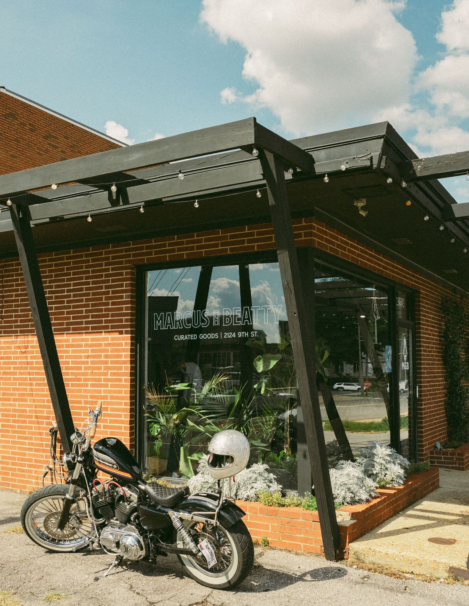 Motorcycle parked outside a brick storefront with black pergola and large windows.
