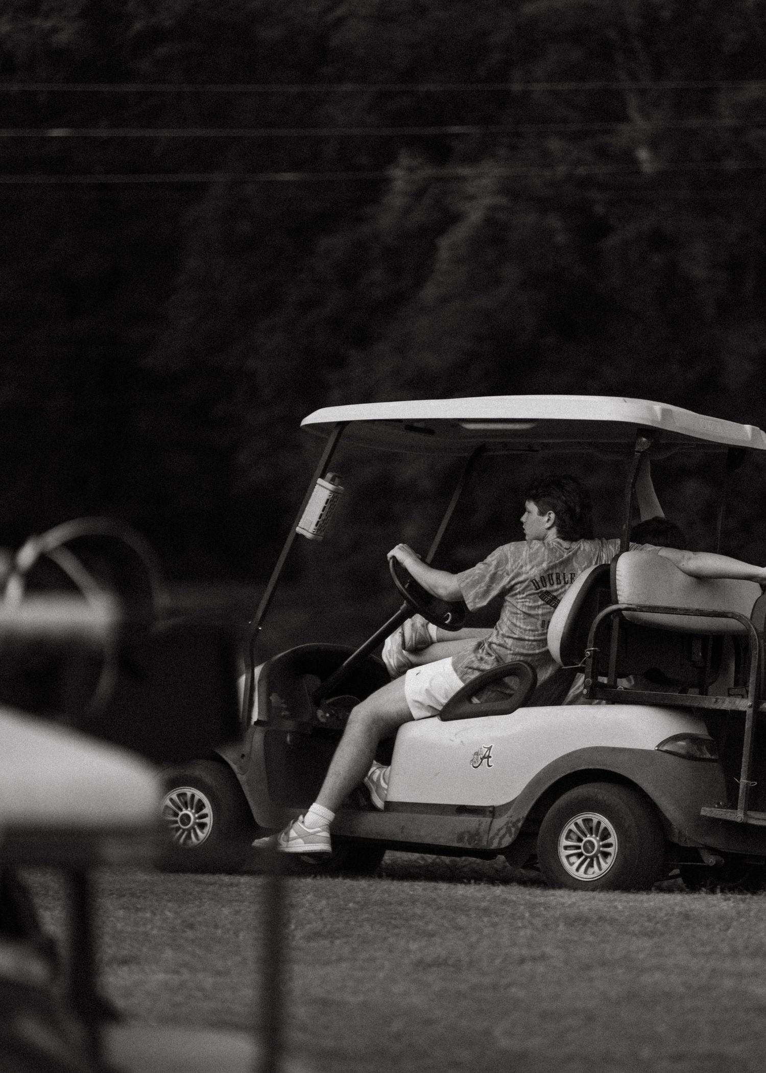 Young man driving a golf cart on a grass course in black and white photo.
