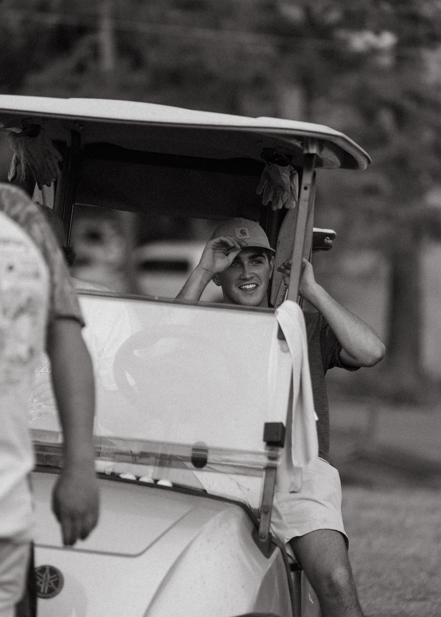 Smiling young man adjusting his cap while seated in a white golf cart.