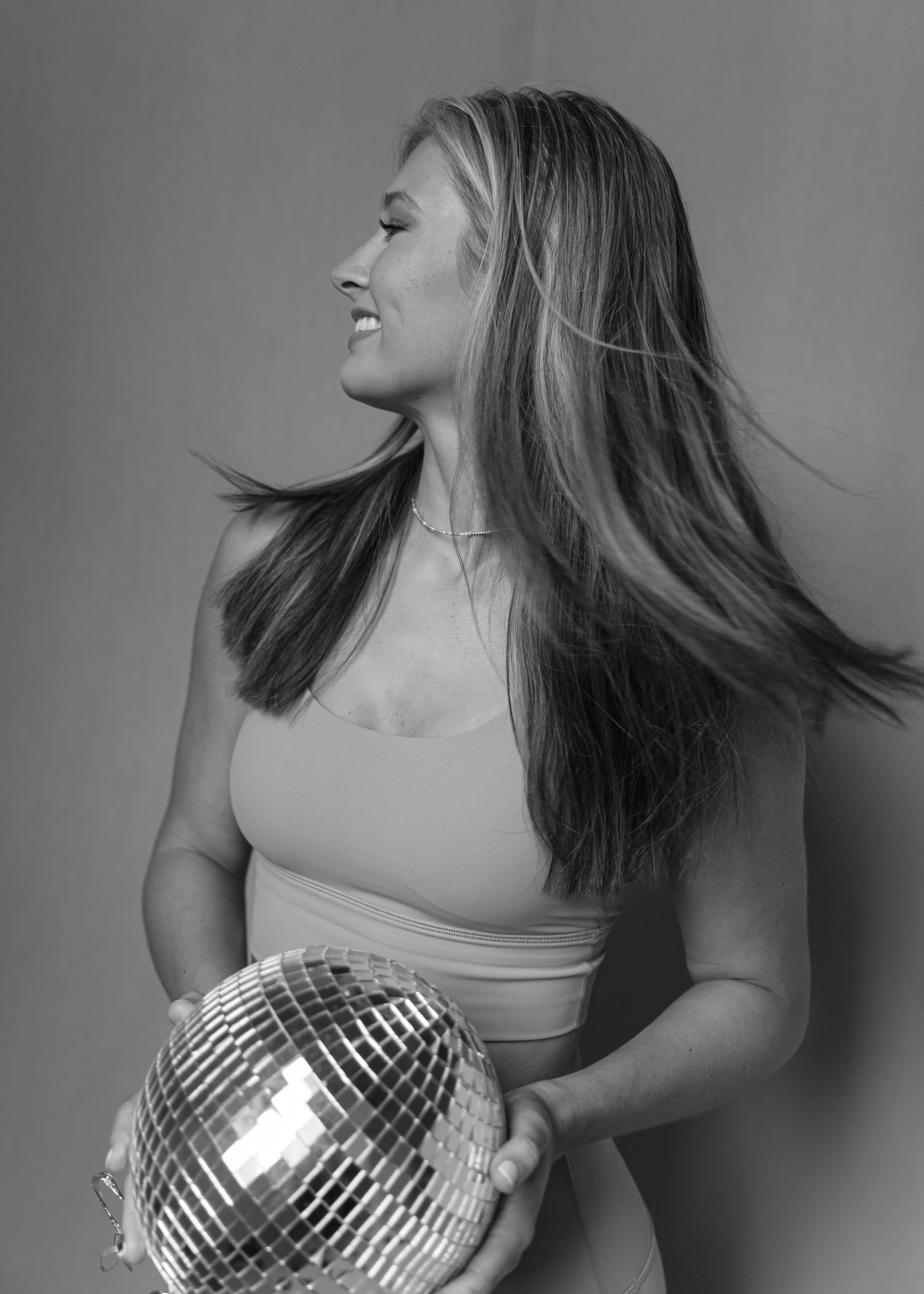 Black and white photo of woman with flowing hair holding a disco ball, looking away.
