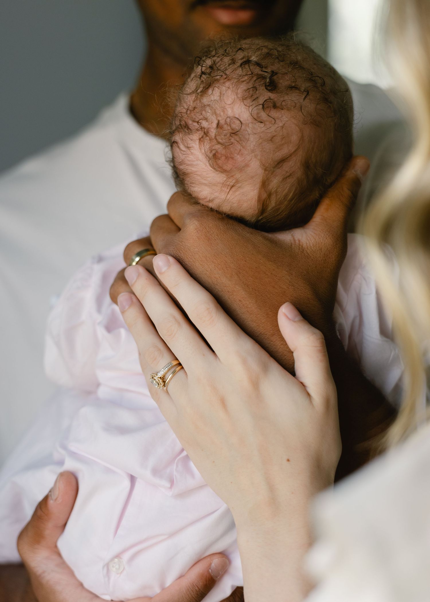 Close-up of interracial couple's hands cradling their newborn baby in pink.
