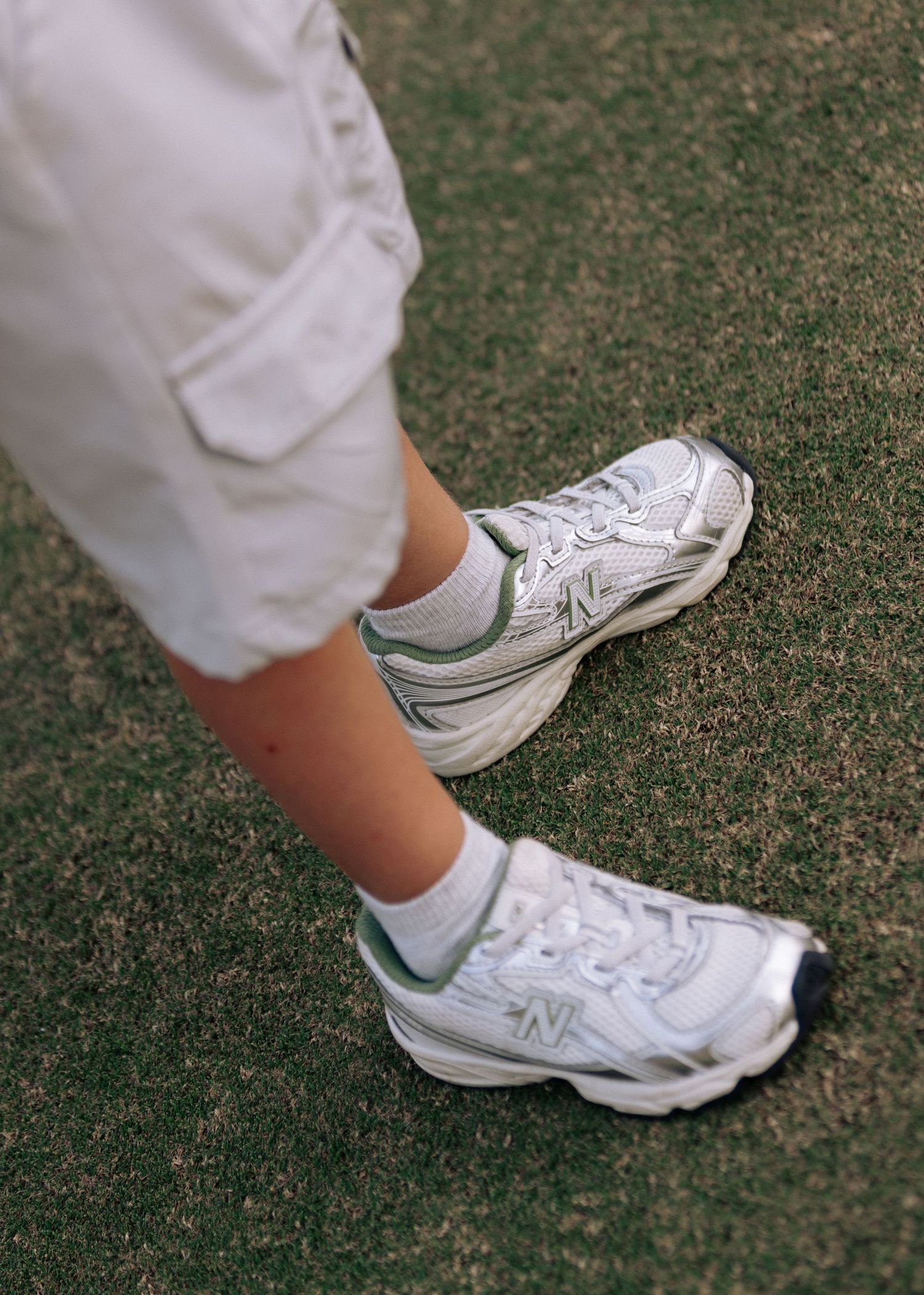 Close-up of white New Balance sneakers worn with white socks on green grass.