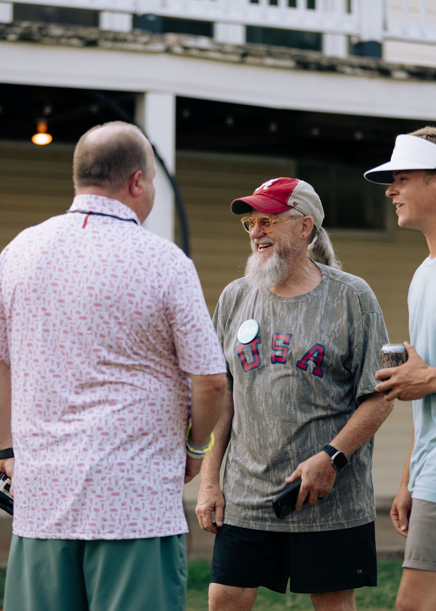 Three men socializing outdoors, one wearing a USA shirt and red cap.