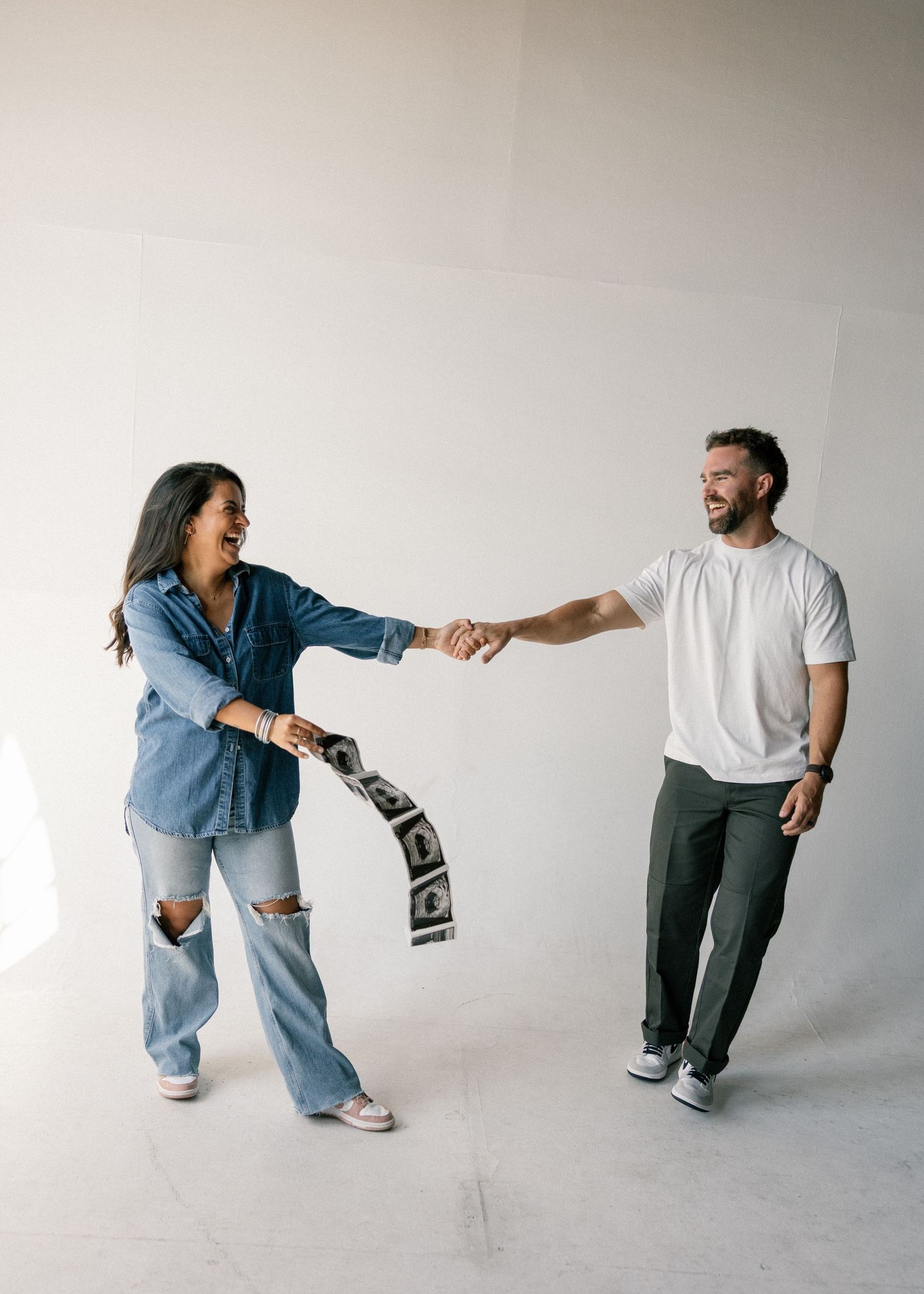 Laughing couple sharing a strip of photo booth pictures in white studio.