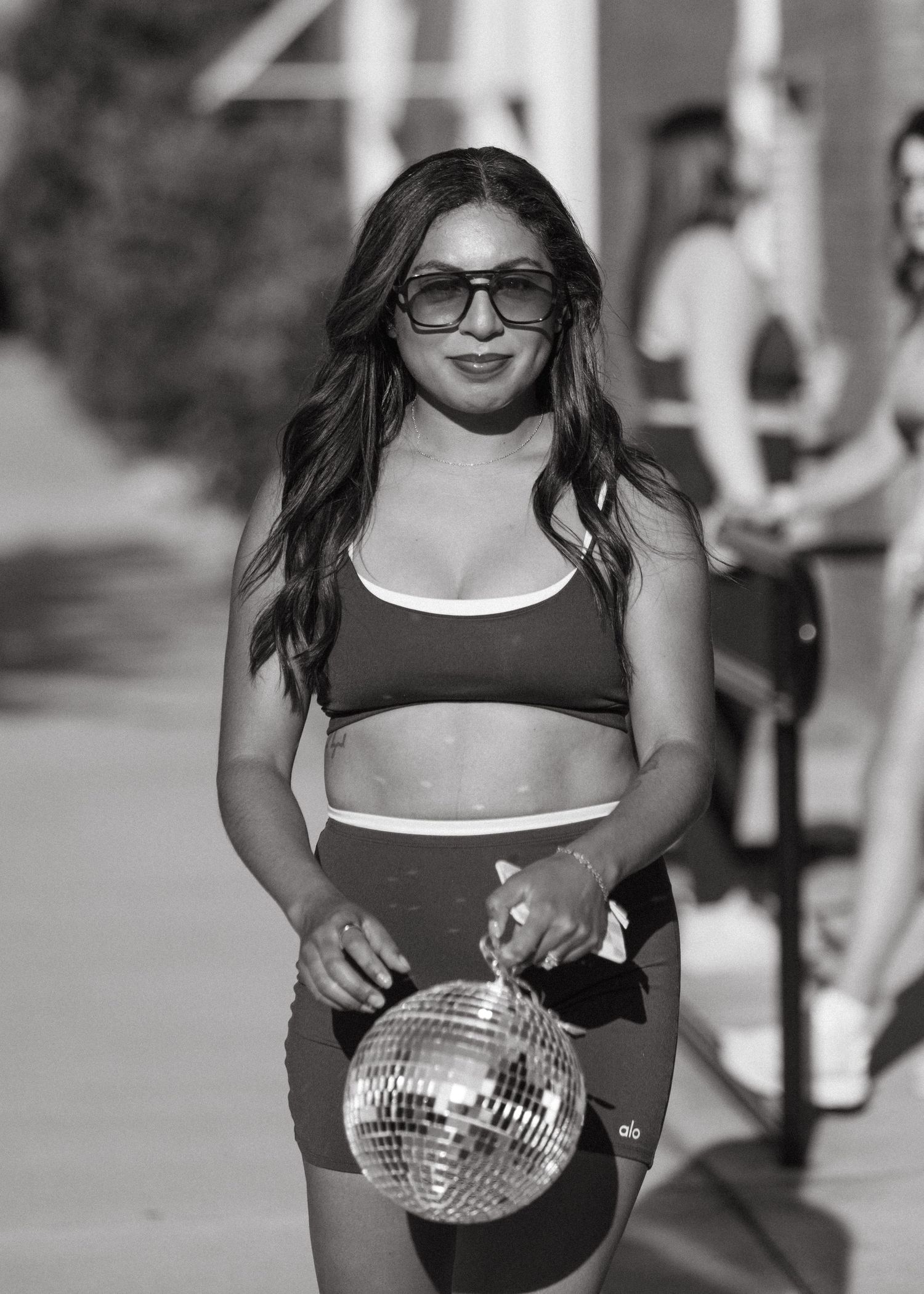 Woman in black sports bra and shorts holding a disco ball outdoors in black and white photo.