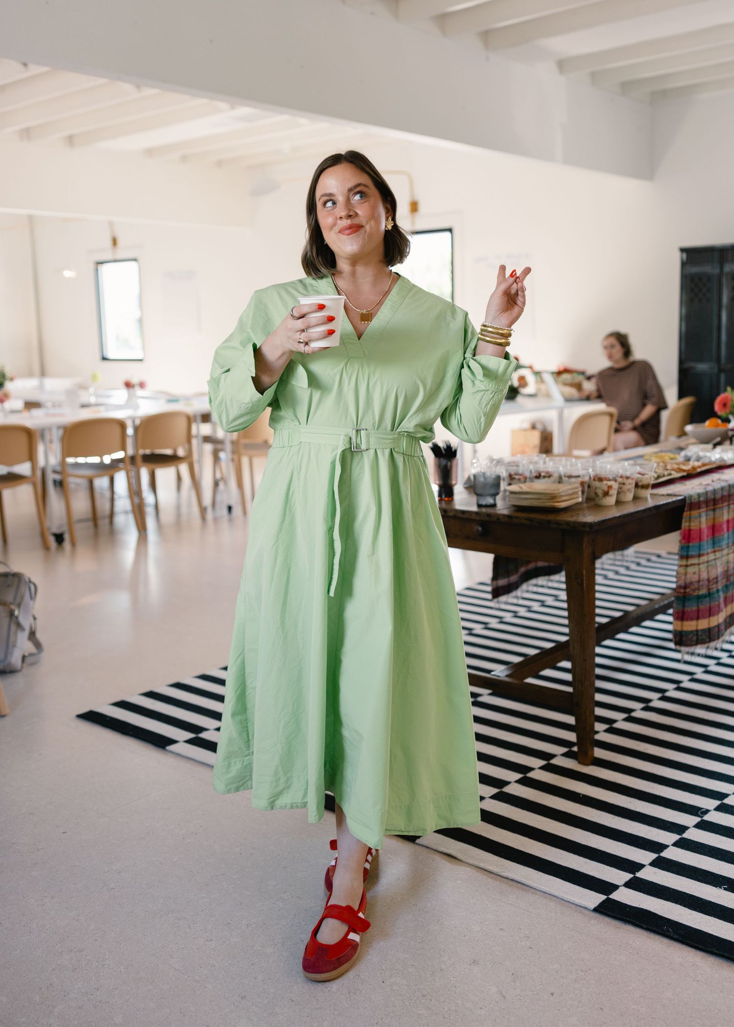 Woman in mint green belted midi dress standing in bright workshop space with striped rug.